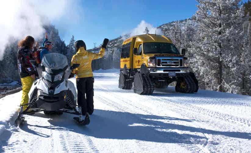 image of a snow machine with 2 people being passed by a snow coach in yellowstone national park in winter.