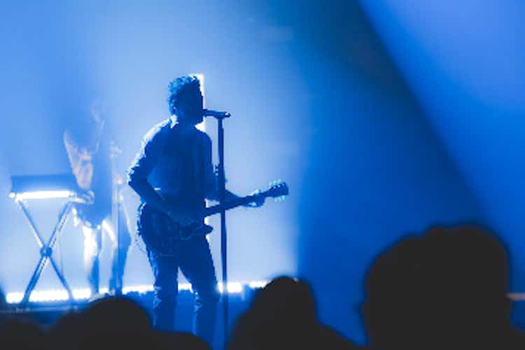 Person playing guitar while singing into a microphone at a concert. 