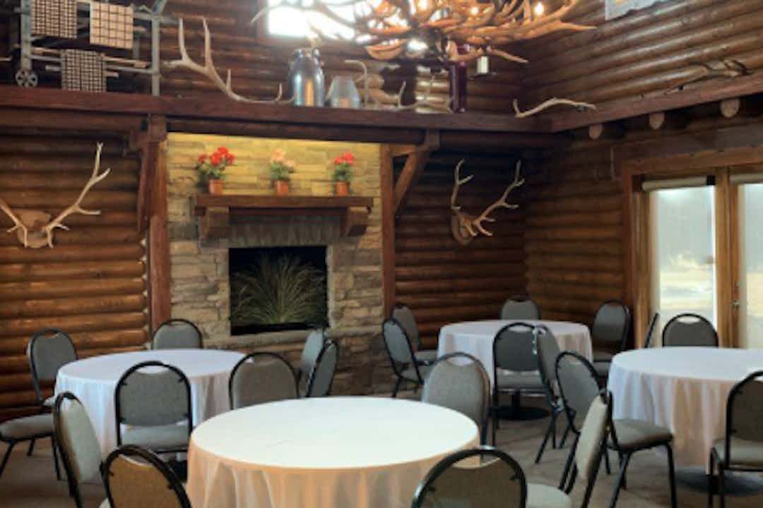 Experience the inviting ambiance of The Loft 475, showcasing a setup of chairs and tables arranged for a reception. The interior exudes a rustic log cabin vibe, complemented by an impressive antler chandelier, creating a warm and welcoming atmosphere.