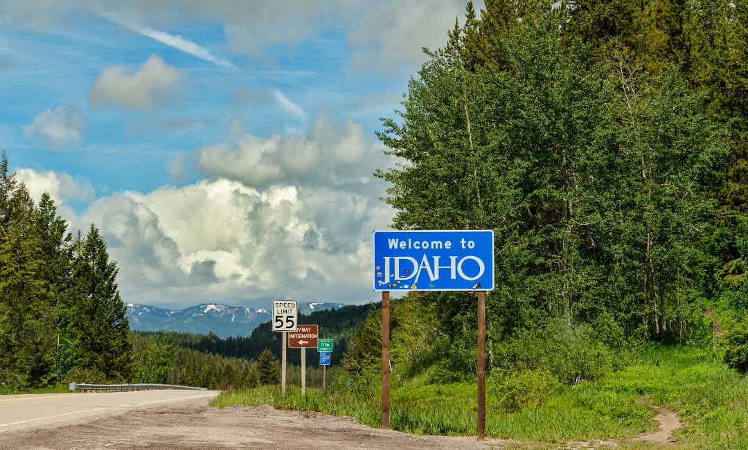 Idaho's state marker between Idaho and Wyoming under blue skies.