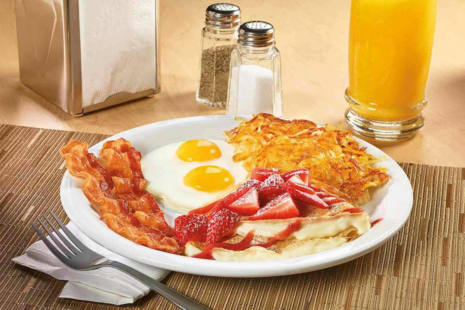 Plate of eggs, hashbrowns, pancakes topped with fresh strawberries, and crispy golden hashbrowns, courtesy of Denny's of Idaho Falls in the Yellowstone Teton Territory.