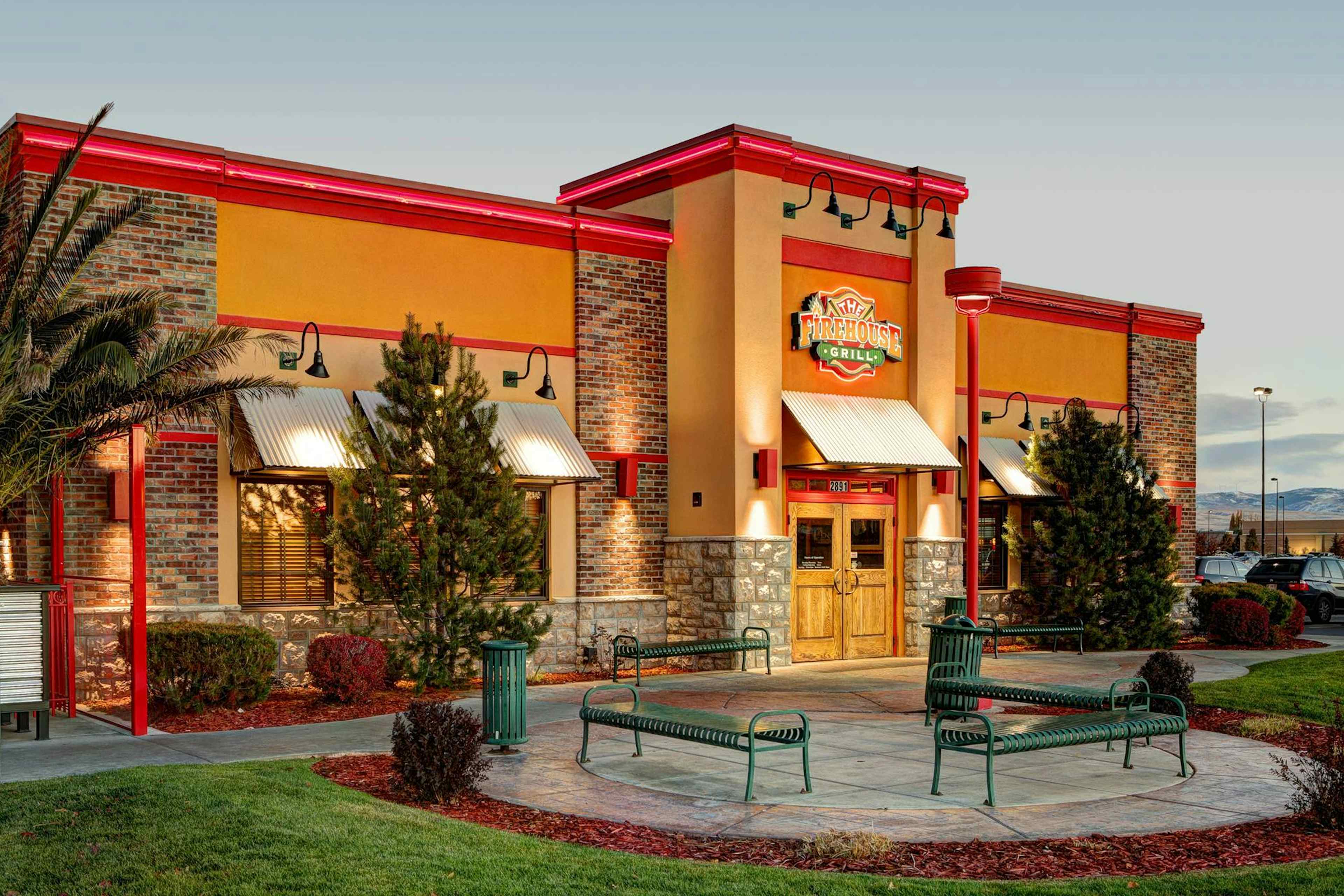 Outside view of the Firehouse Grill, with benches and some trees, during a nice summer night.