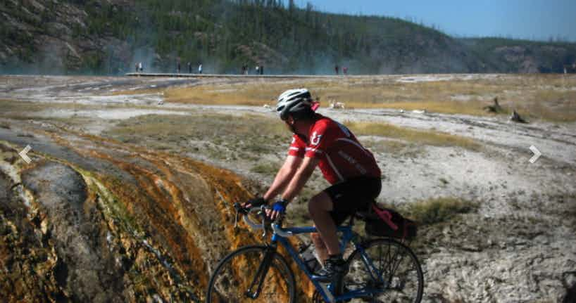 Cyclist next to Old Faithful in Yellowstone National Park in Yellowstone Teton Territory.