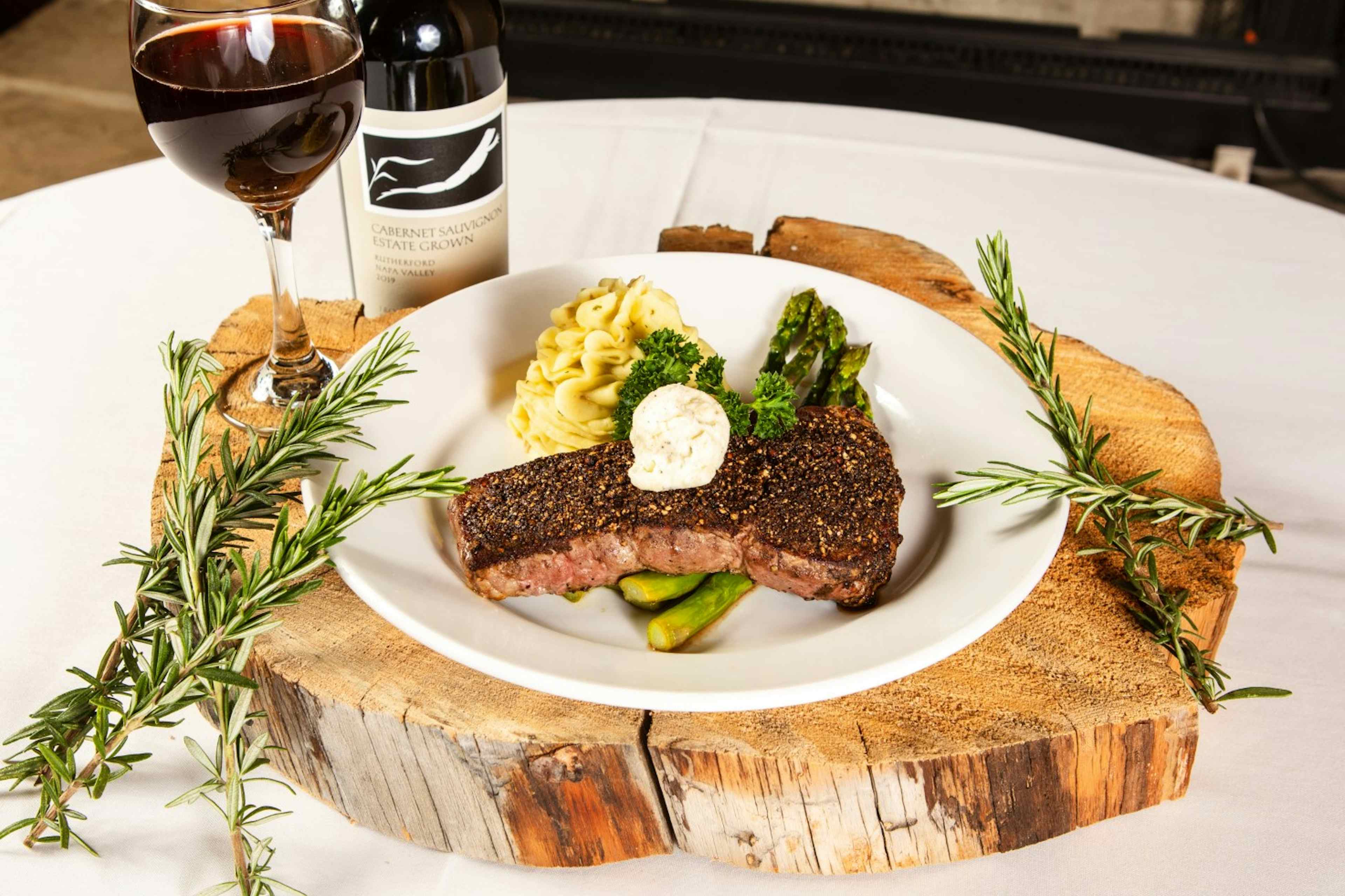 Steak with mashed potatoes and asparagus, served with a glass of red wine, offered at the Flying Saddle Steakhouse.