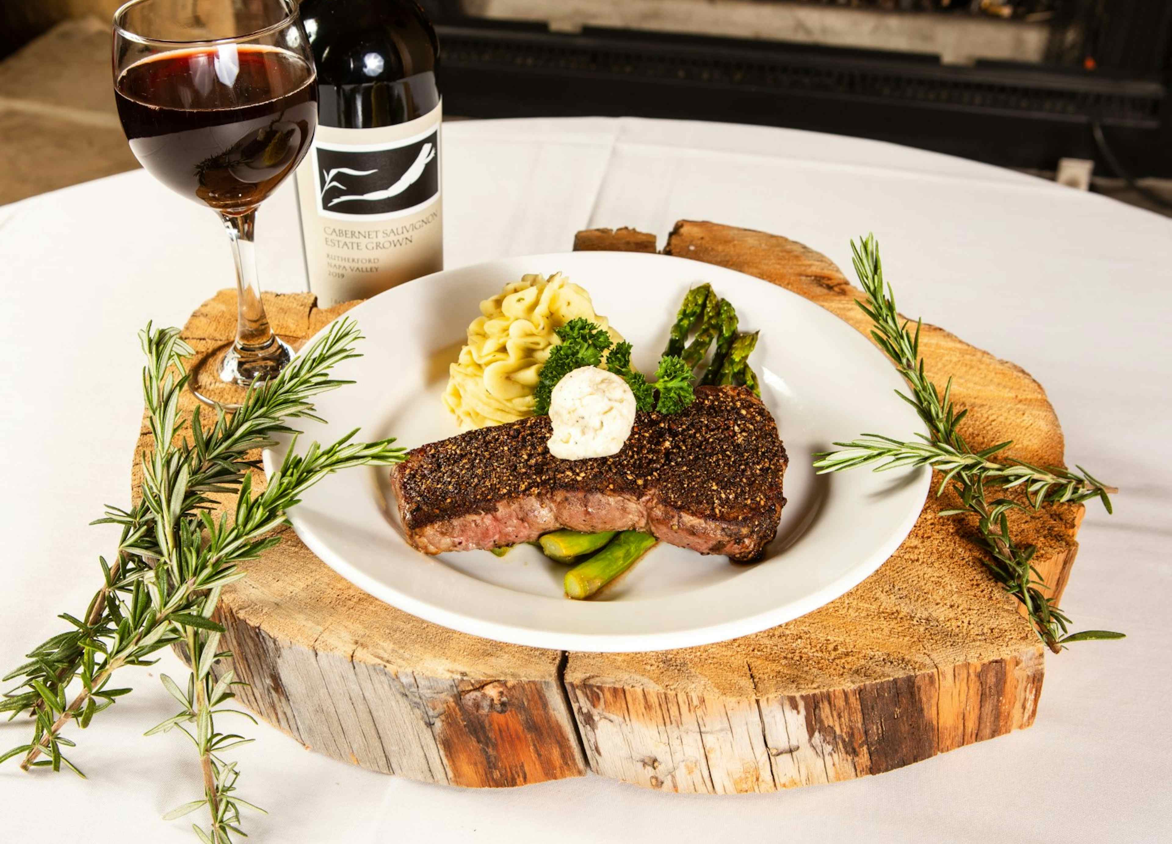 Steak with mashed potatoes and asparagus, served with a glass of red wine, offered at the Flying Saddle Steakhouse.