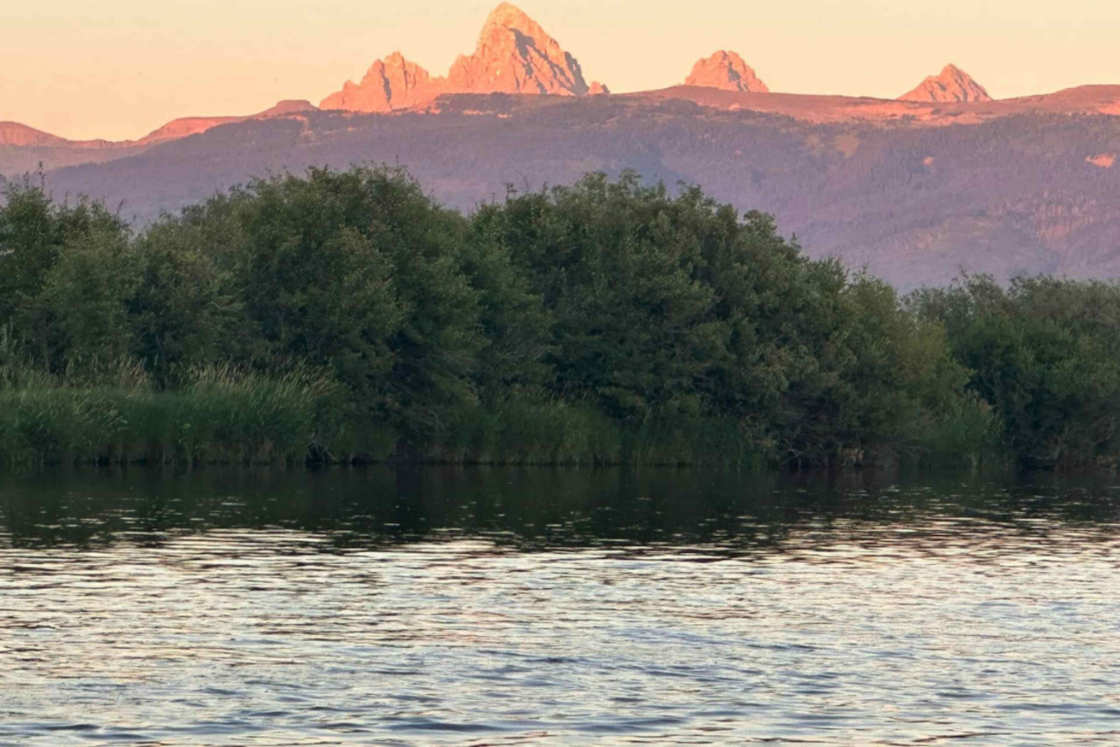 Picture of alpenglow on the Grand Teton and Teton Mountain Range from the Teton River in Teton Valley, a part of Eastern Idaho and Yellowstone Teton Territory.