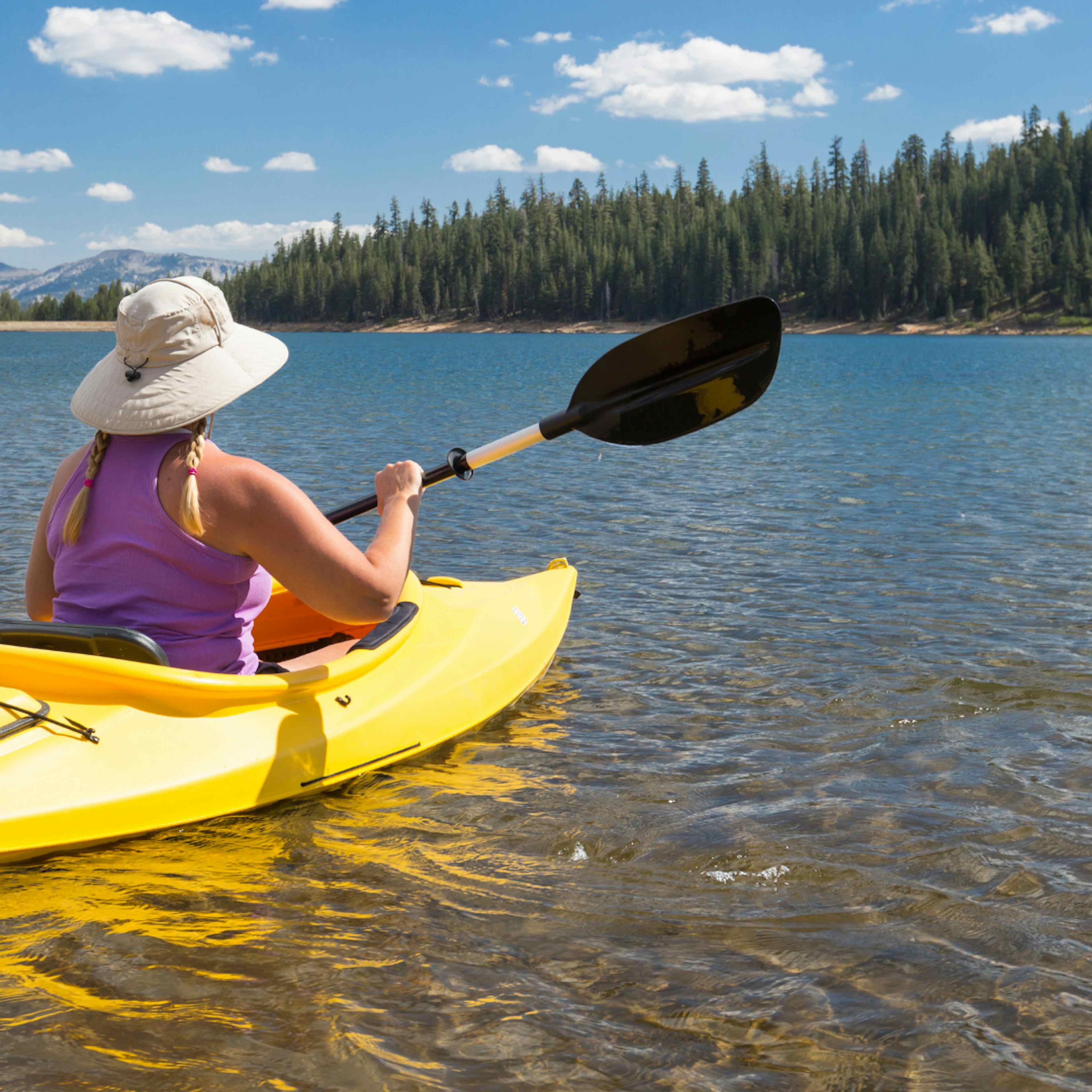 Woman paddleboards on Henry's Lake in Henry's Lake State Park in Island Park, ID in Yellowstone Teton Territory.