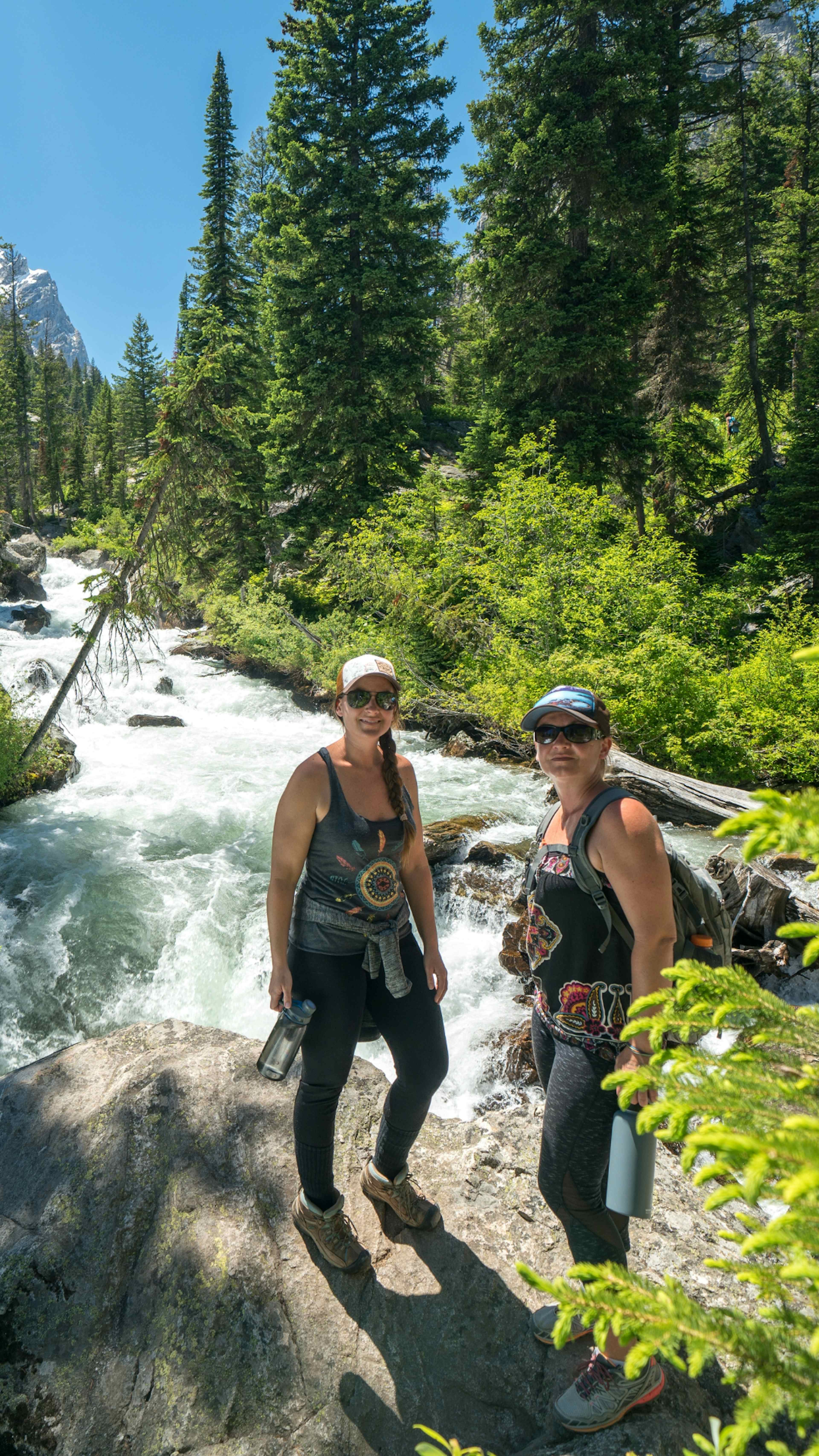 Two hikers stand next to Cascade Falls in Grand Teton National Park.