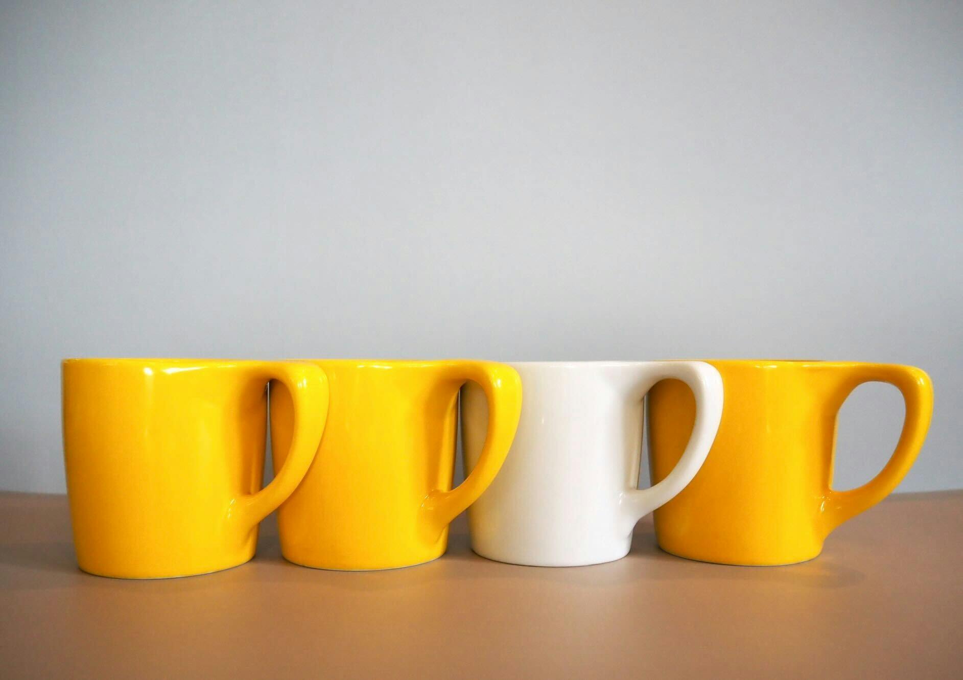 Four mugs neatly lined up. Three mugs are bright yellow while one in the middle right is white.