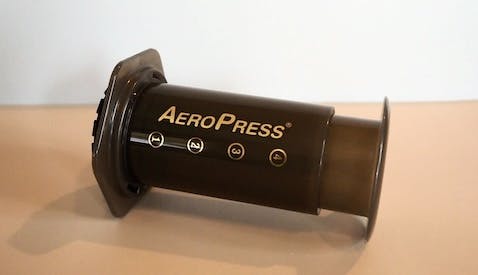 An AeroPress coffee brewer. It is made out of black plastic and is a cylinder shaped plunger with a filter on the end.
