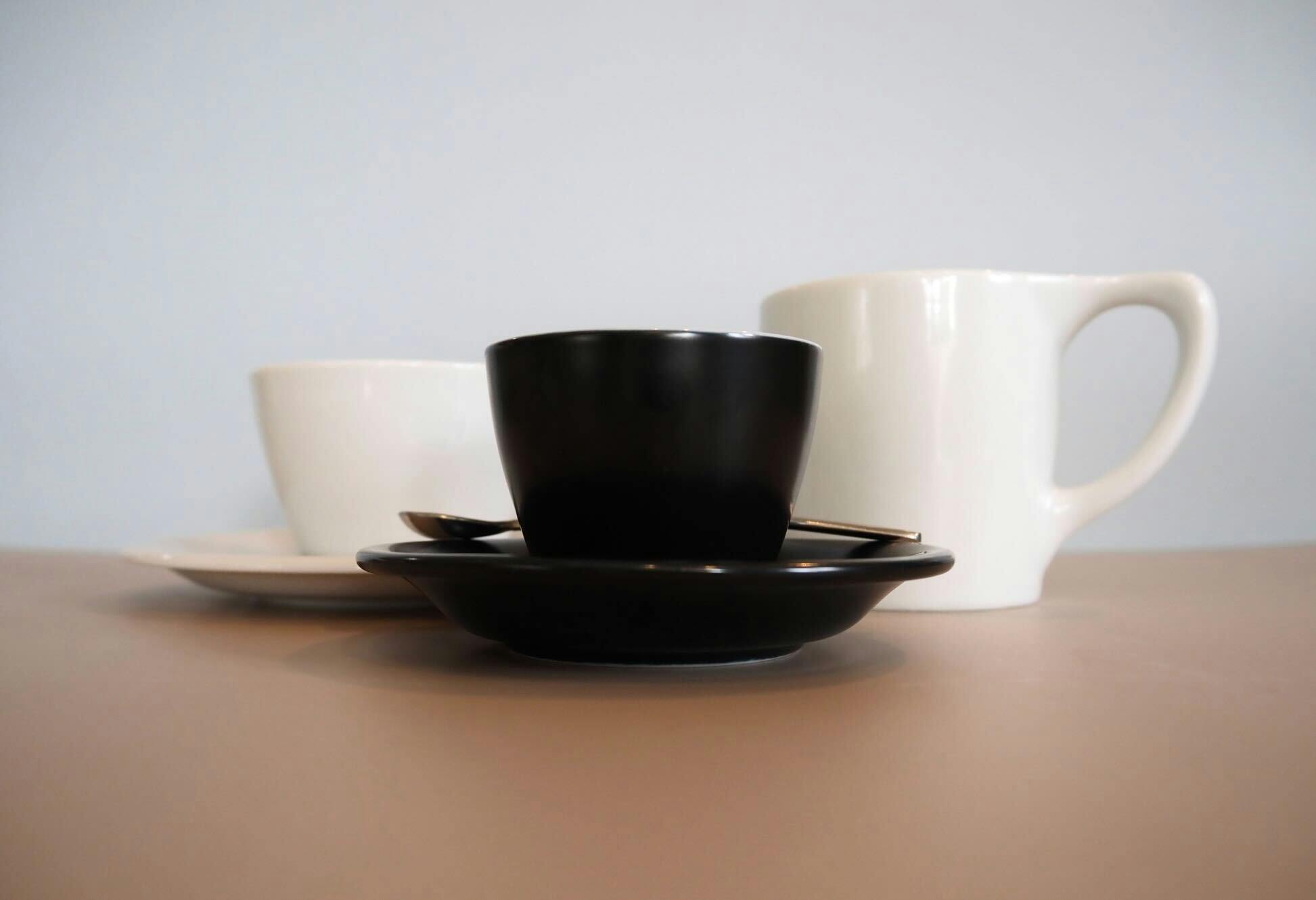 An assortment of white coffee cups with a black espresso cup in the front.