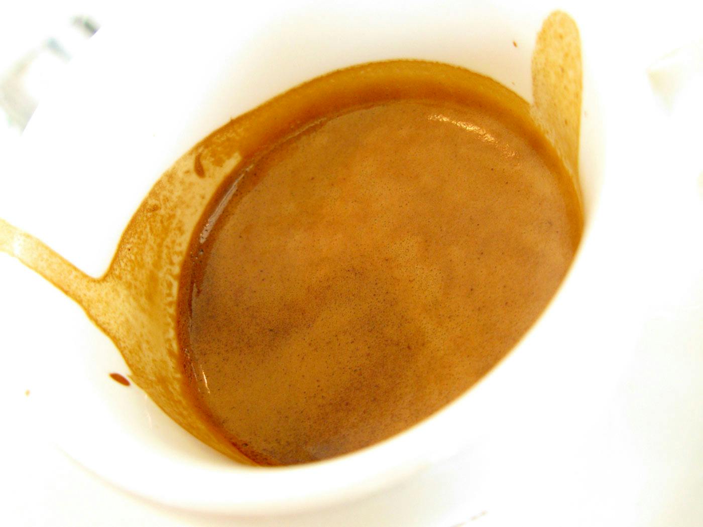 close up photo of a golden brown freshly pulled shot of espresso in a white demitasse.