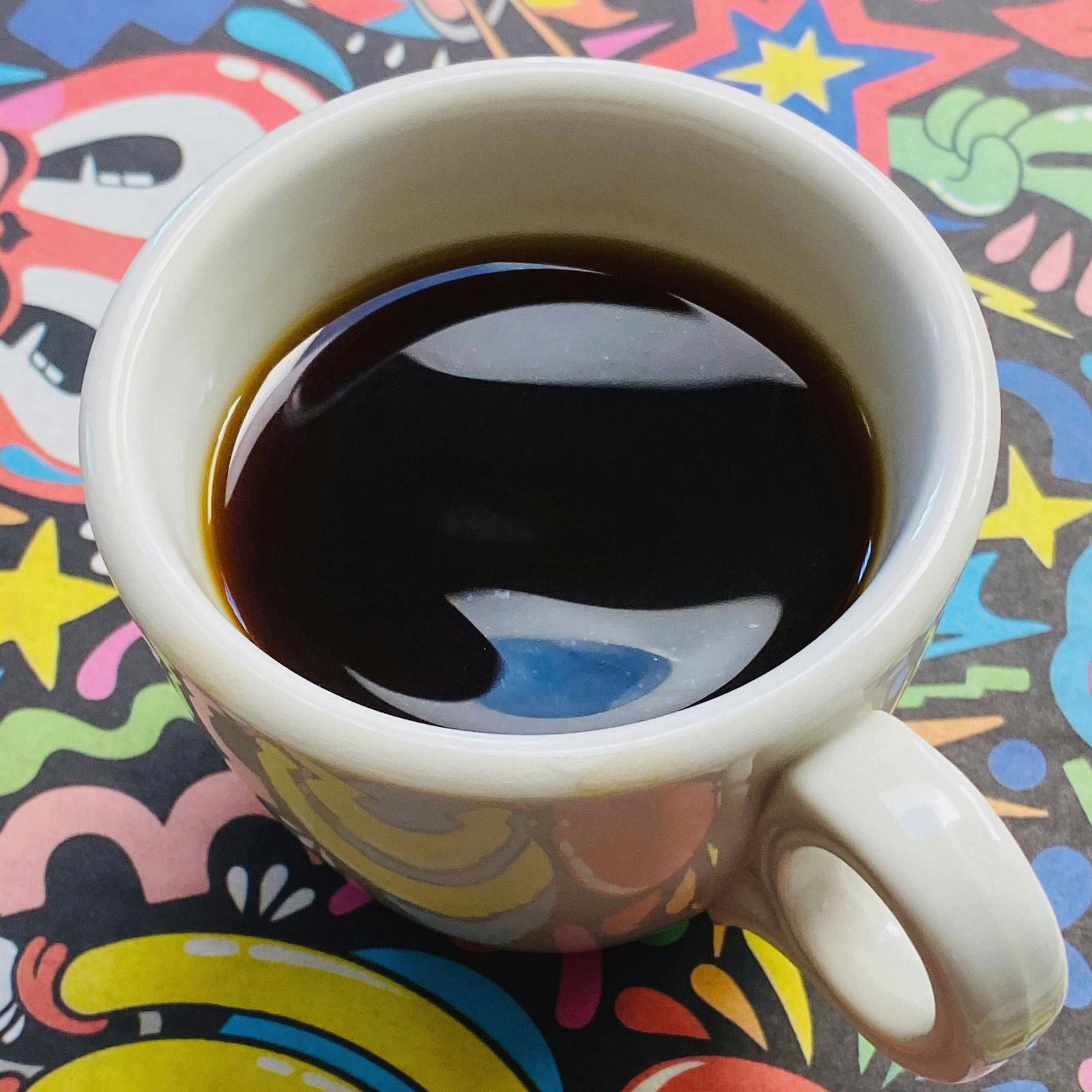 A hot cup of YES PLZ Coffee with a colorful background
