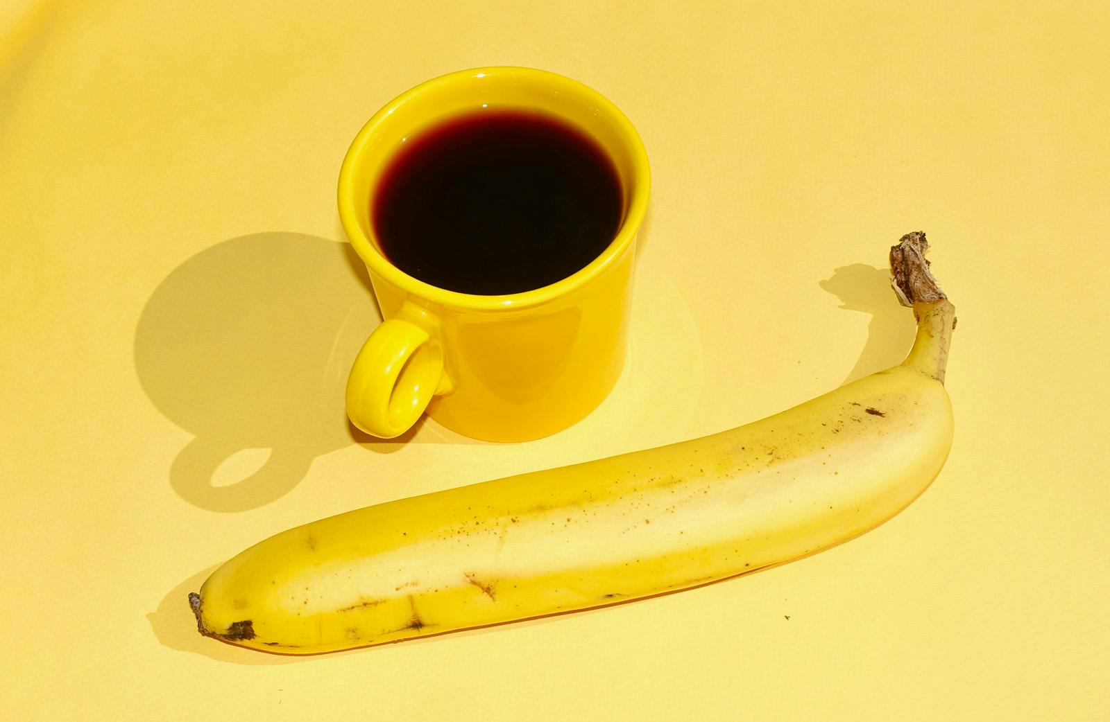 a yellow fiestaware mug of yes plz coffee and a banana on a yellow background