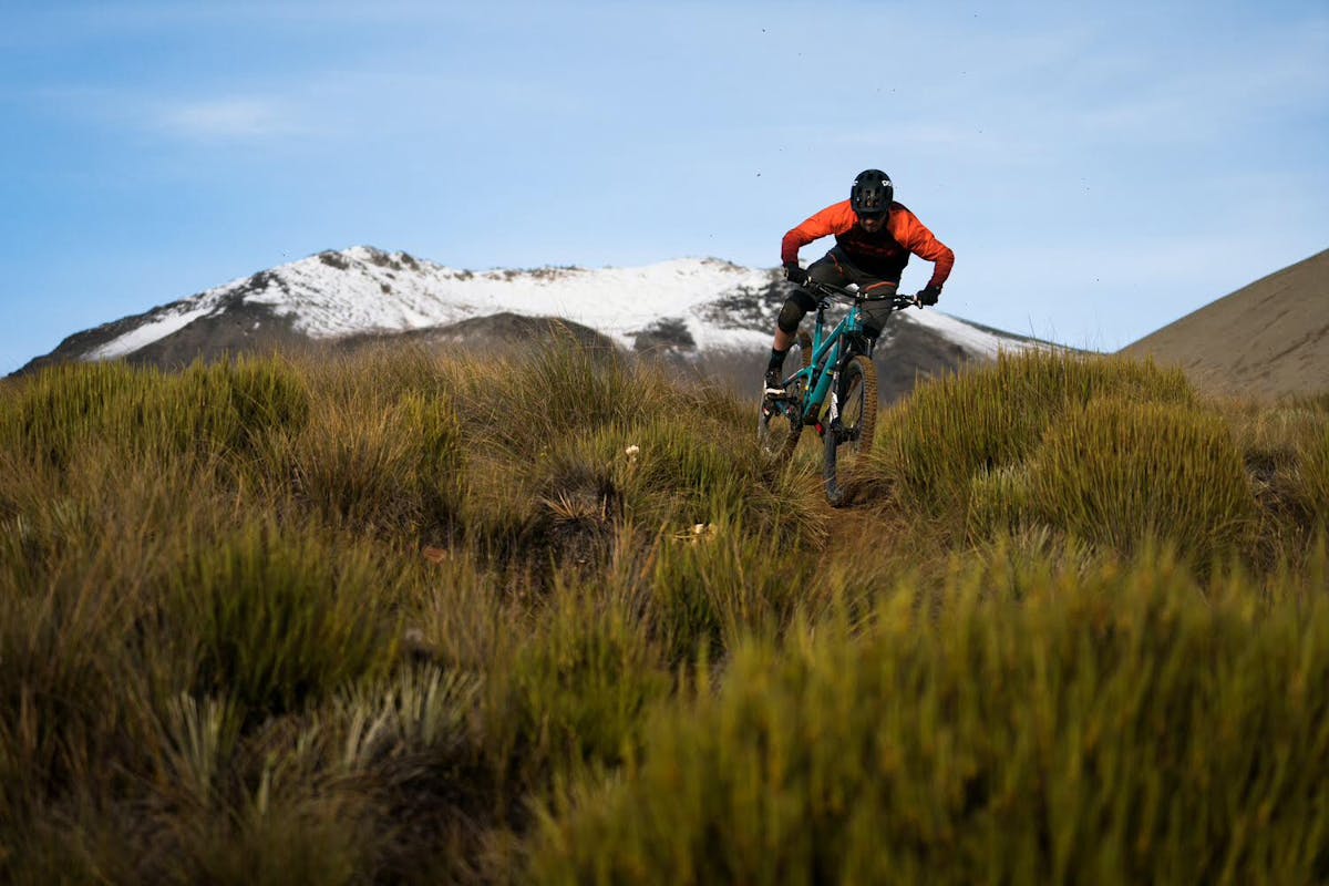 Tom Sampson riding tight, grassy single track with a mountain in the background