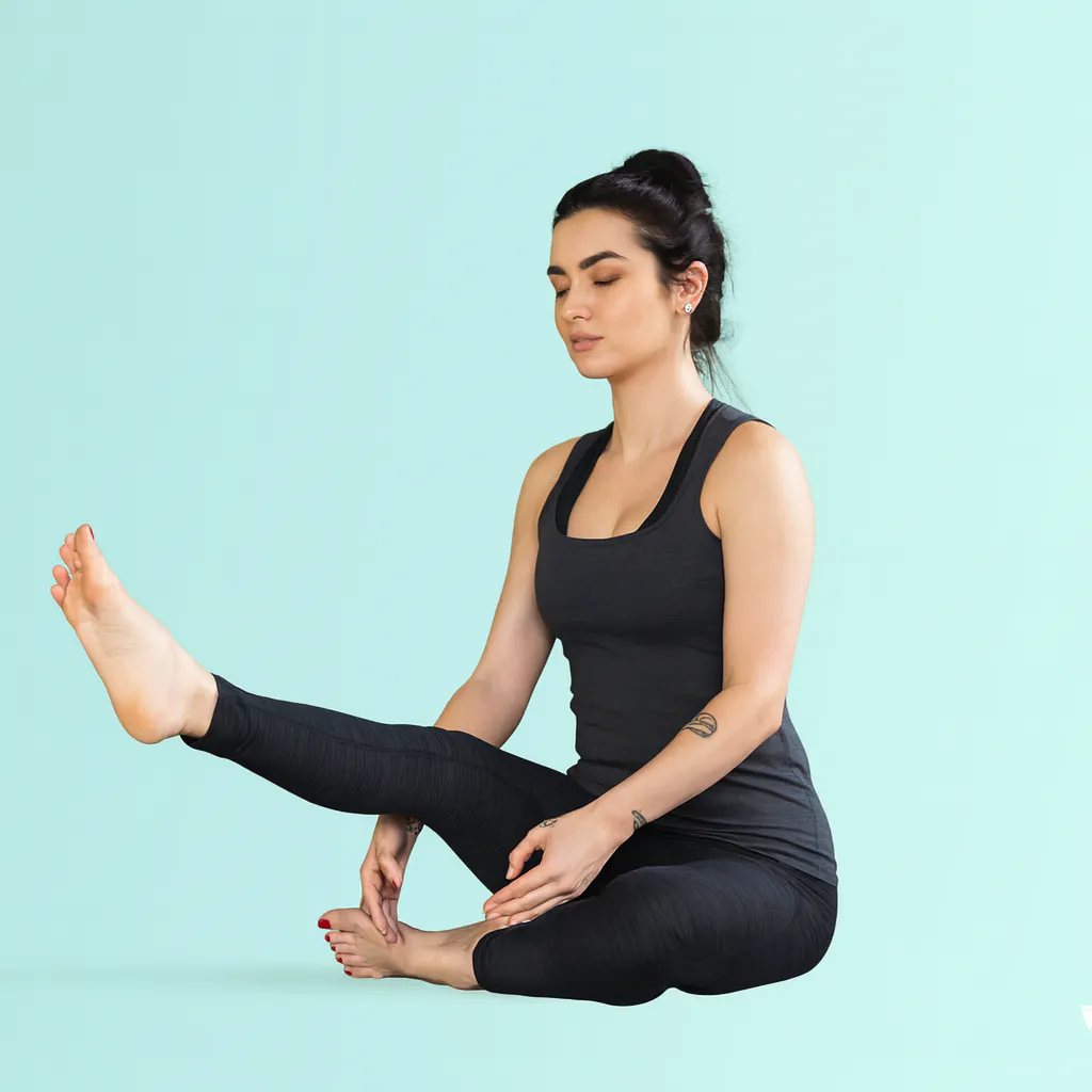 Studio portrait showing a person in seated yoga position demonstrating the release and reset phase of Heron Pose, with one leg lowering in controlled movement against a mint green backdrop