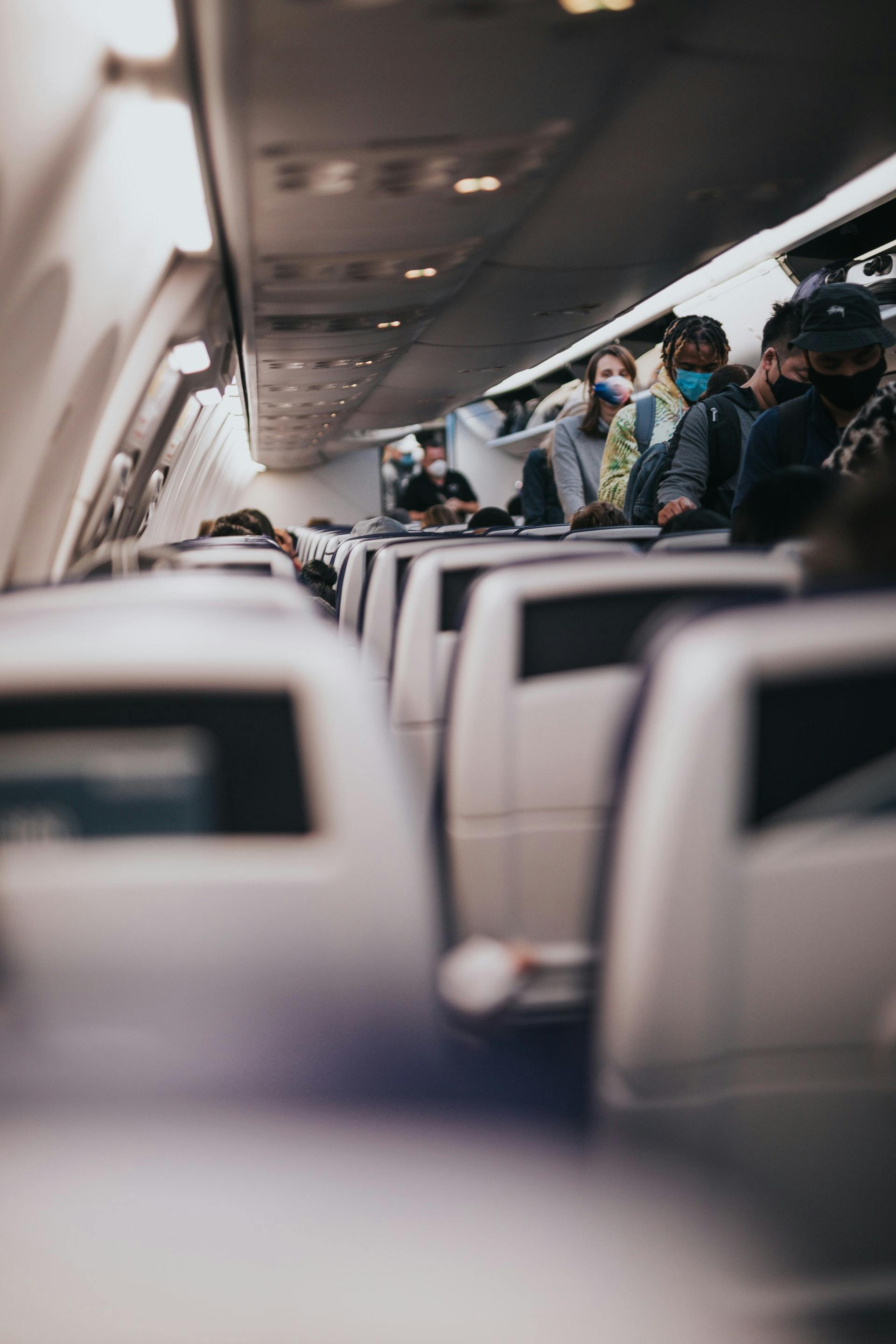 A queue of passengers are standing in the centre aisle of a plane