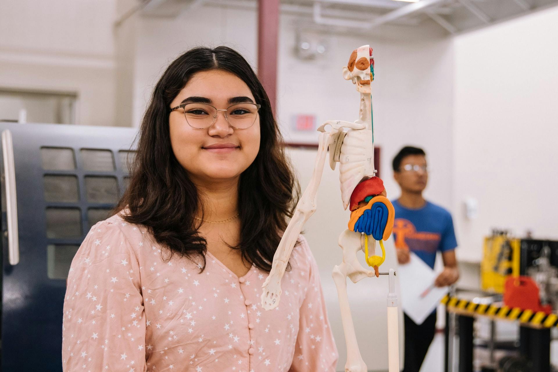 A smiling lady sits behind a model of the human body