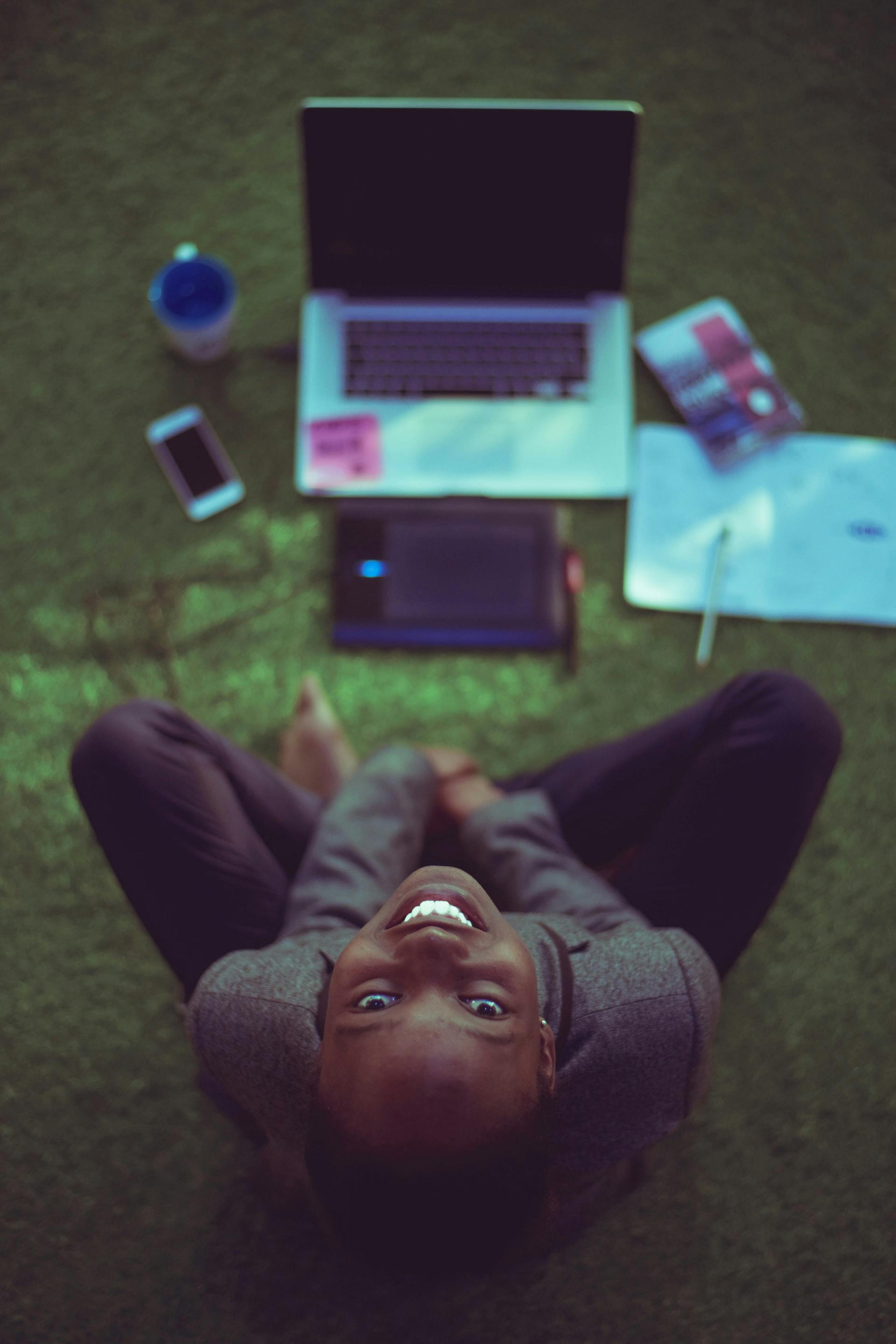 A lady, sitting on the floor, looks up.  In front of her there is a laptop, phone and notepad. 