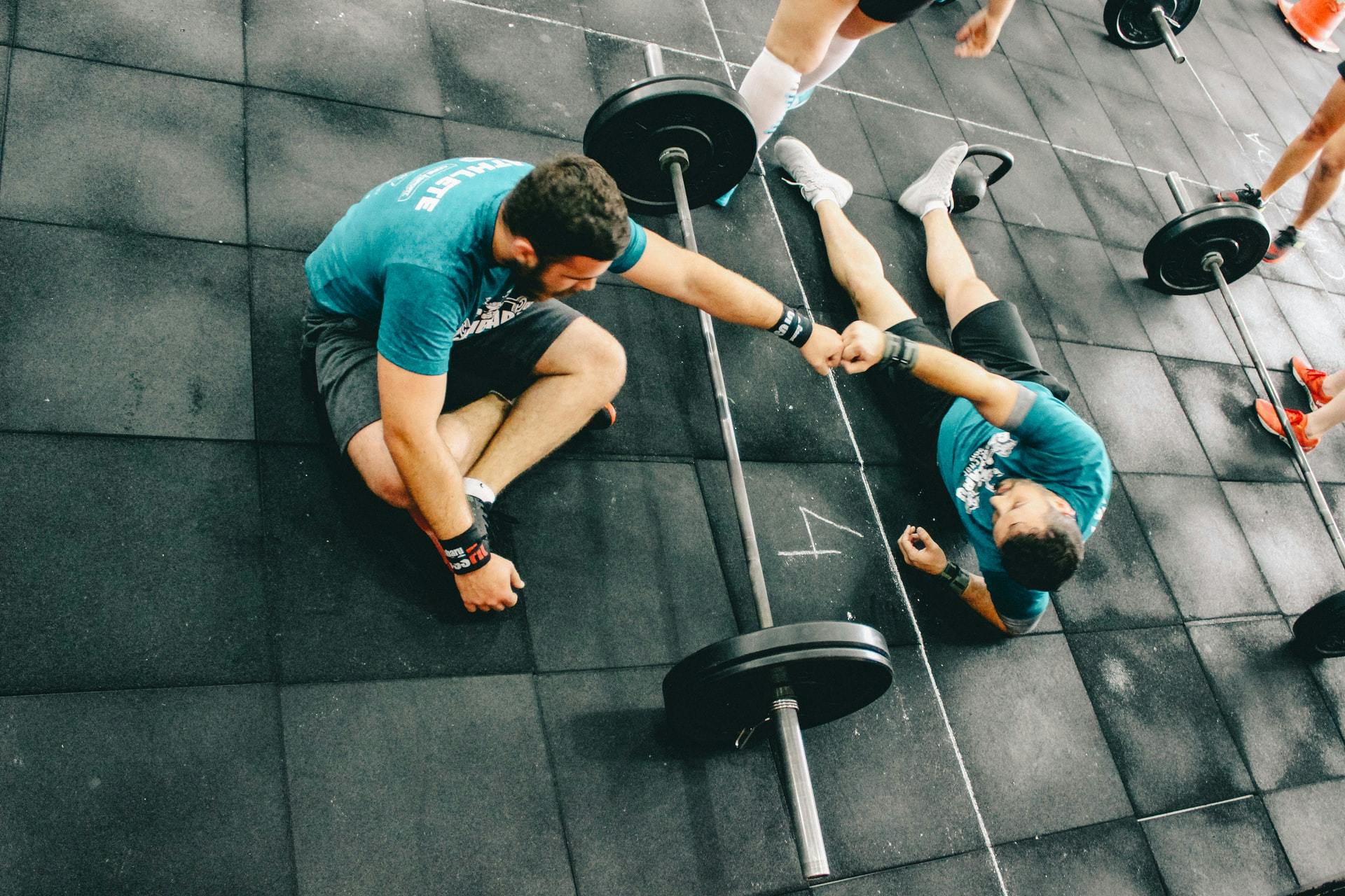 Two men touch fists over a barbell on the floor