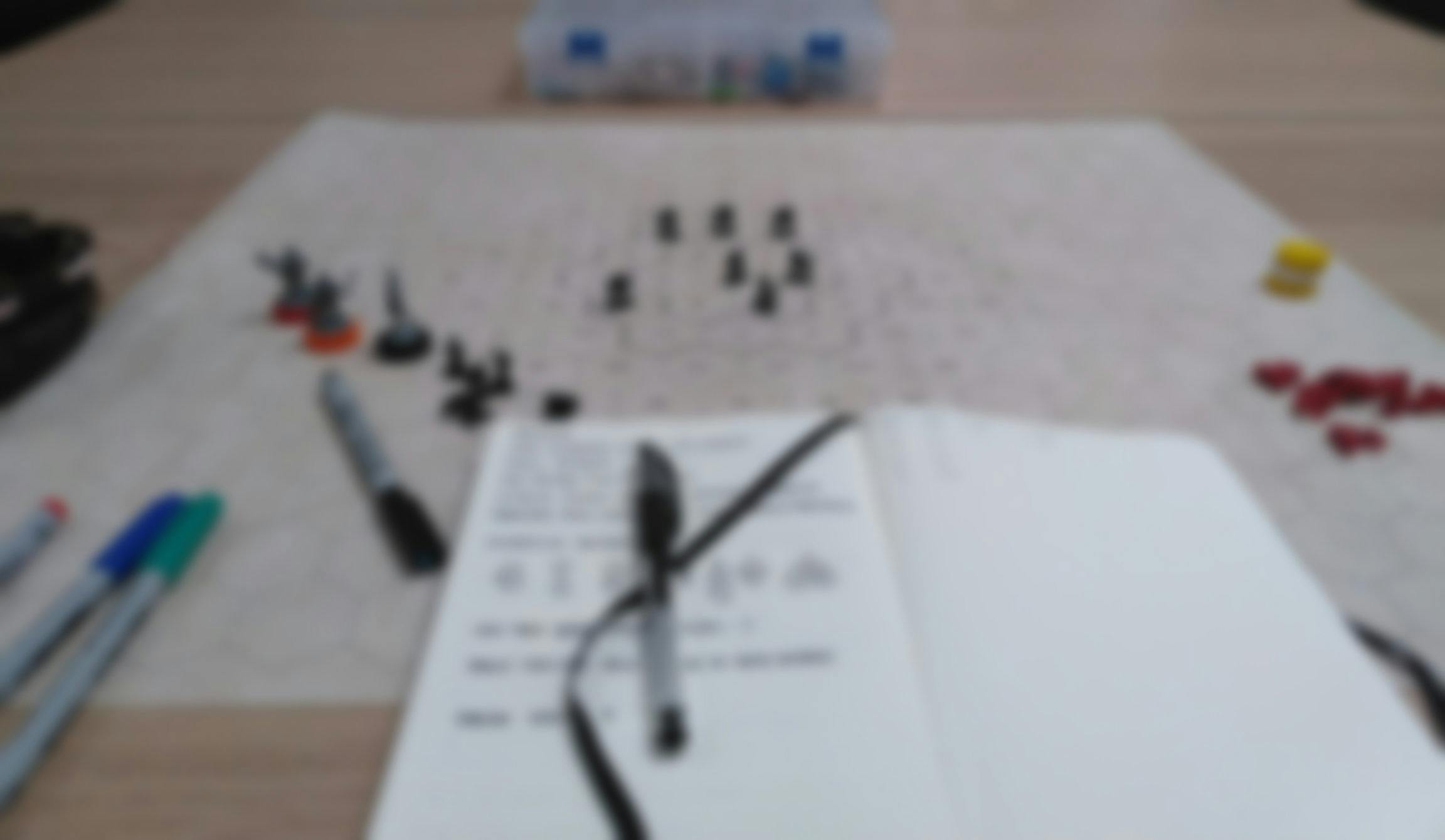A blurred image of a notebook and boardgame pieces on graph paper