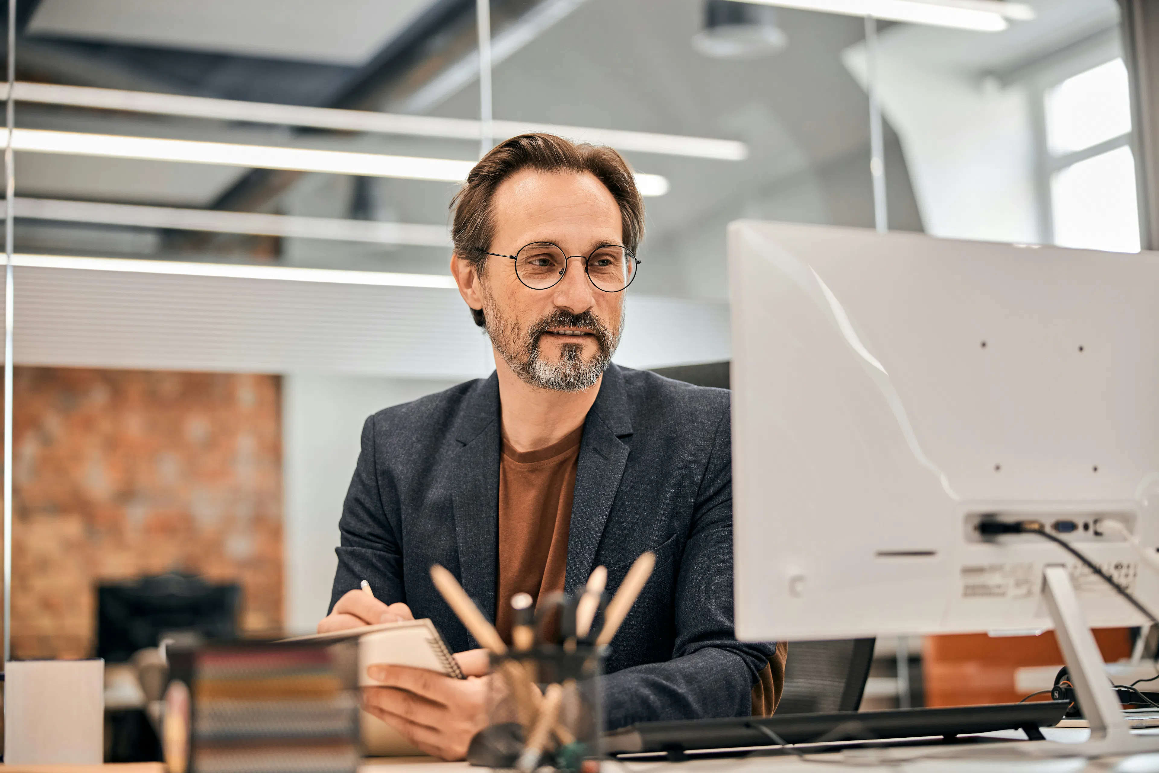 Man taking notes at a desk while looking at a computer monitor.