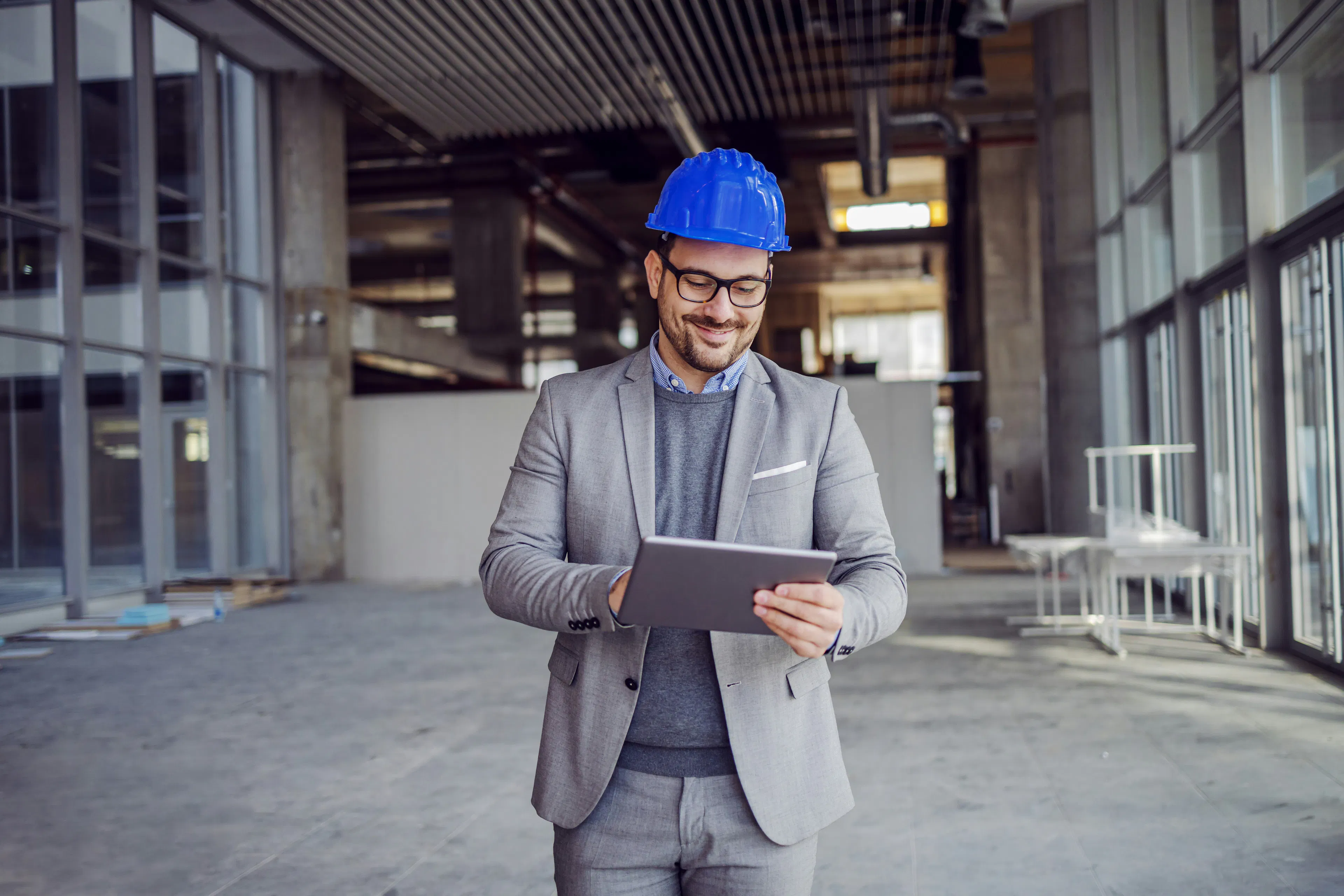 Man in grey suit and blue hard hat holding a tablet