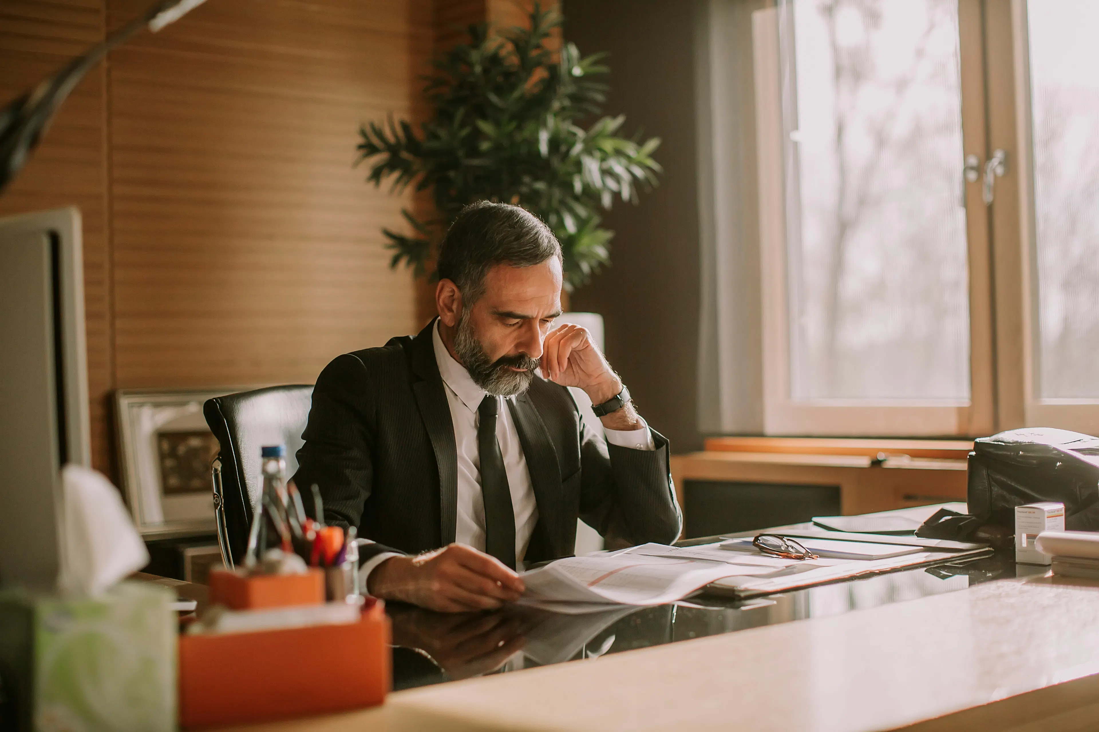 Man in a suit reading documents at an office desk