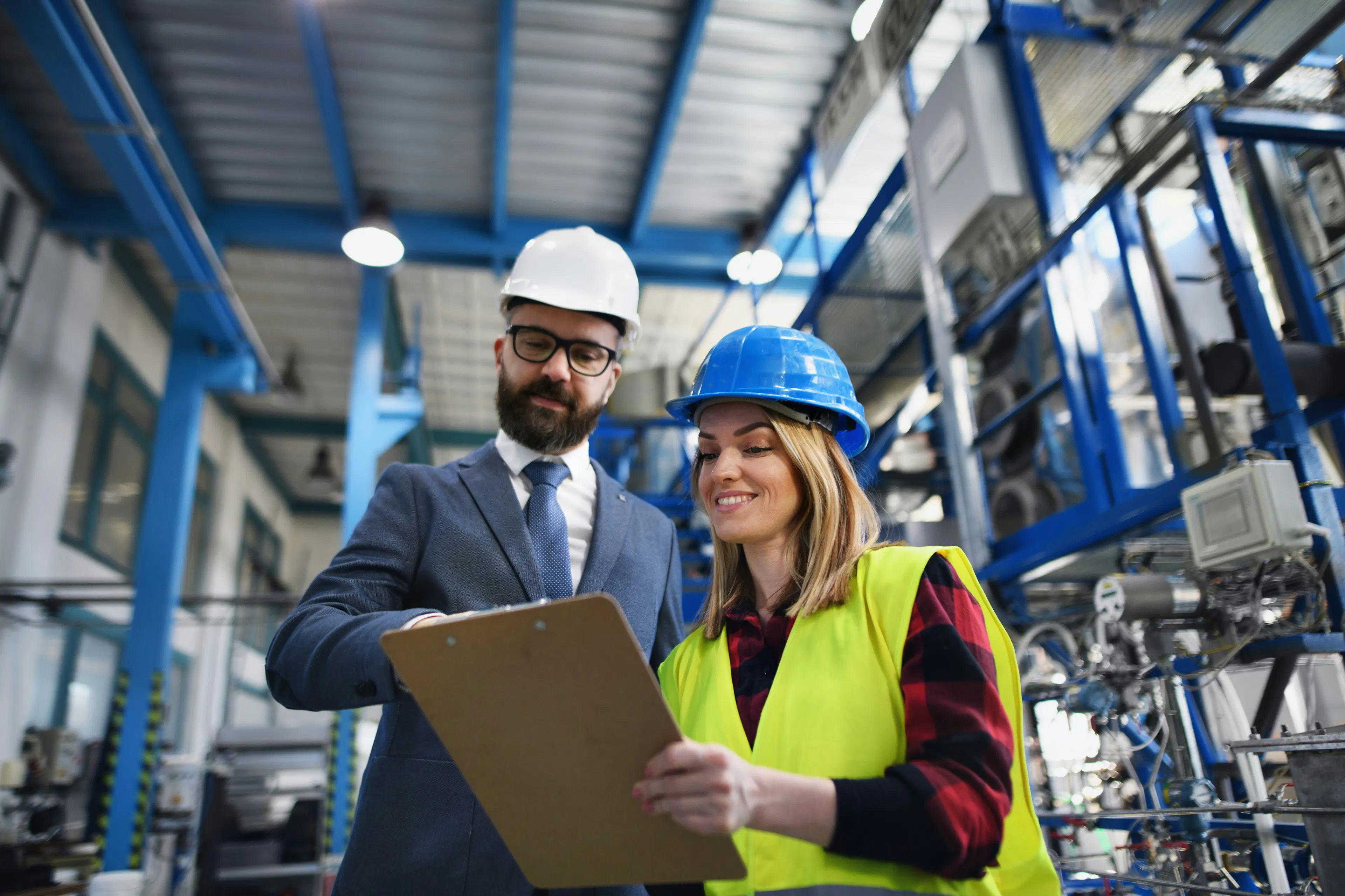 Manager and worker in hard hats reviewing a clipboard in a factory
