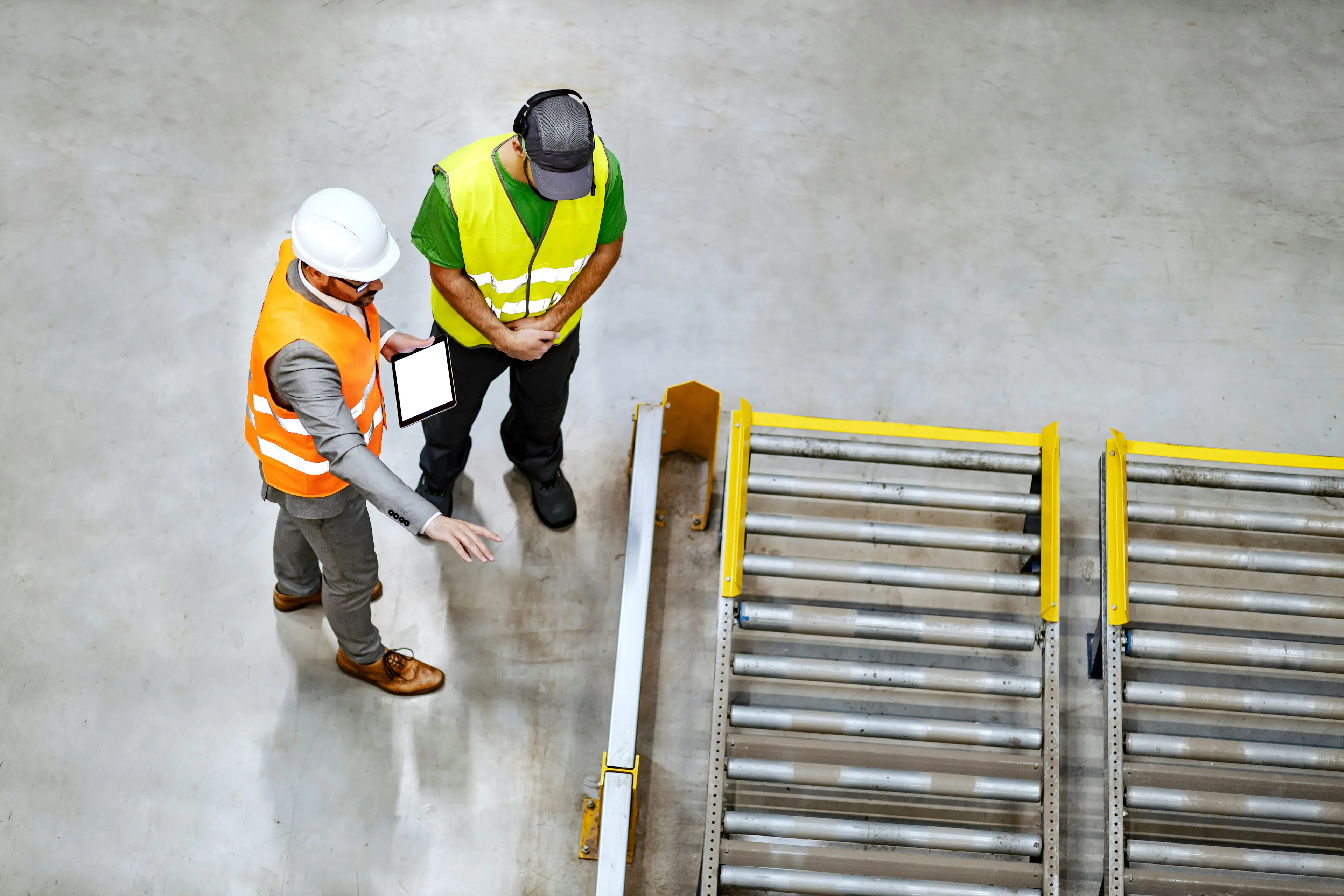 Two warehouse workers in high visibility vests talking.