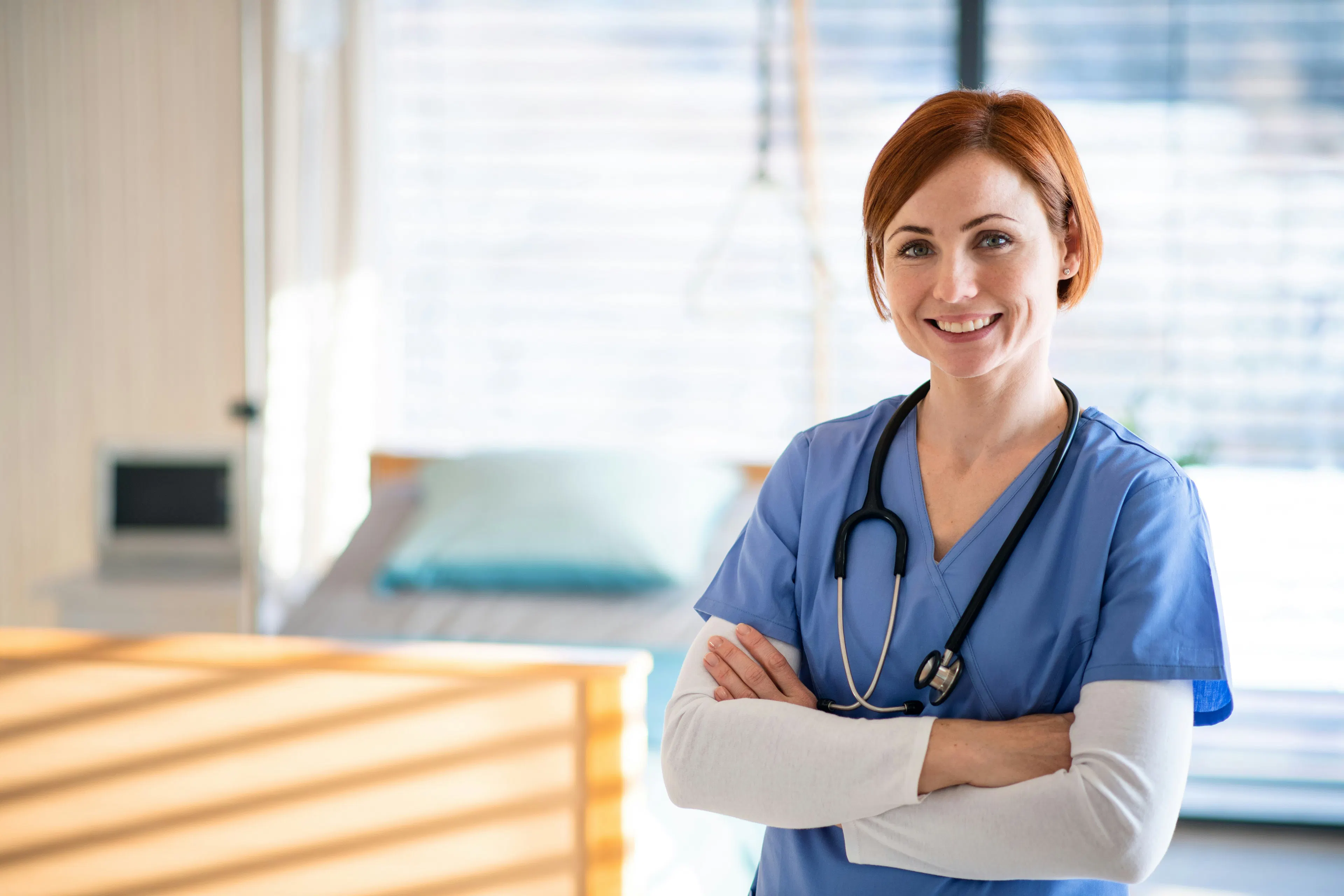 Nurse in blue scrubs standing in hospital patient room.