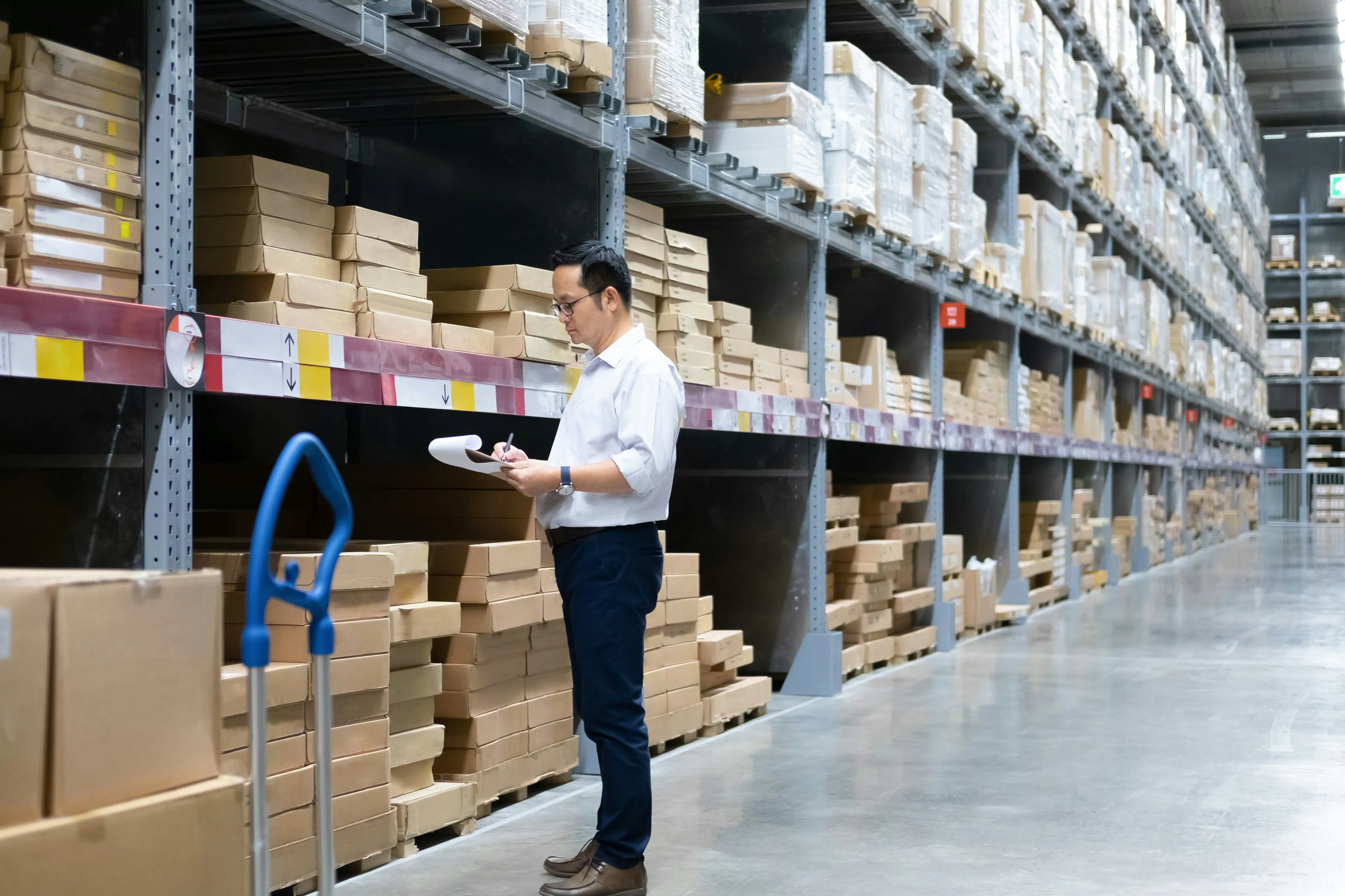 Supervisor writing on a clipboard beside warehouse racking.
