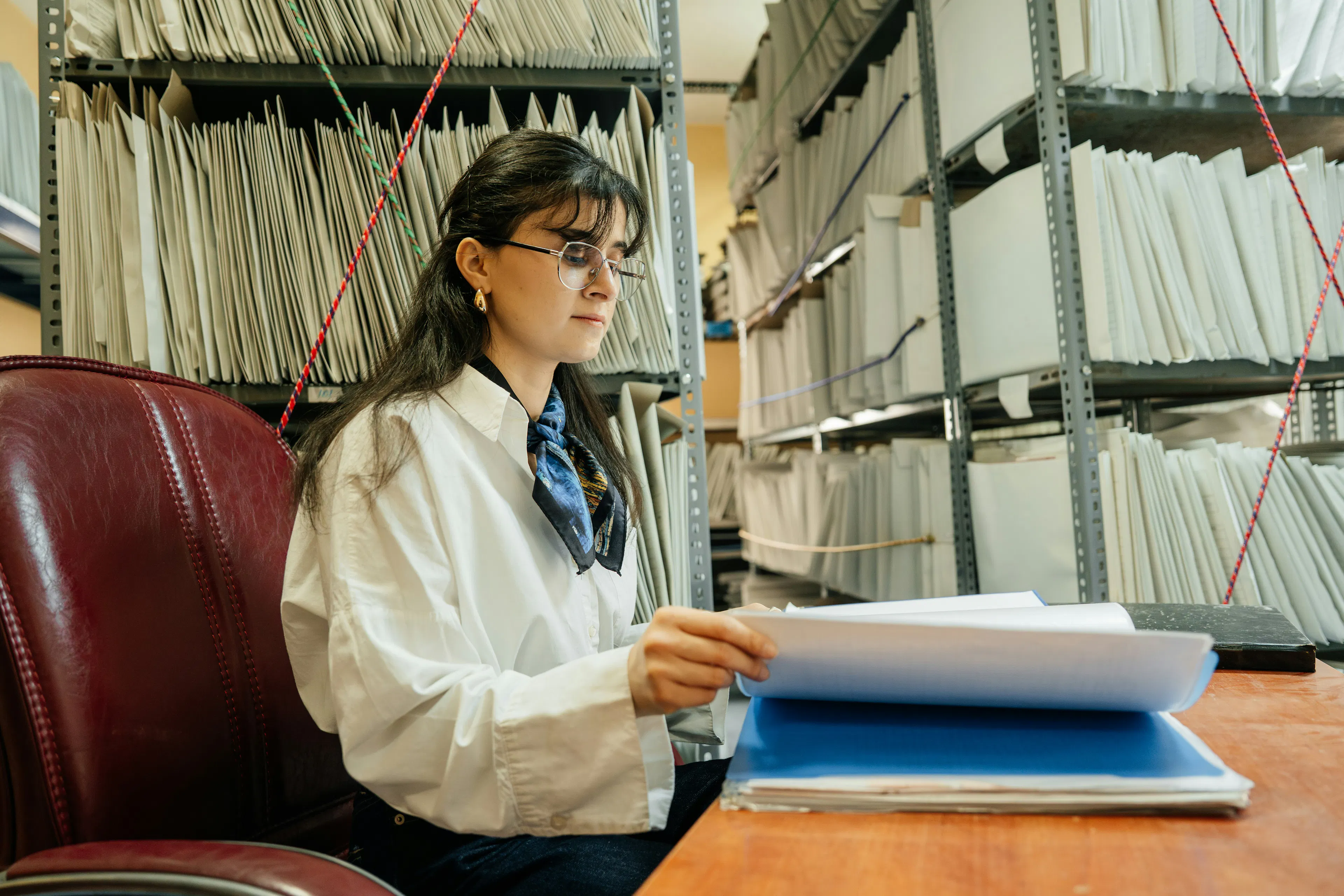 Woman at a desk holding papers beside shelves of files