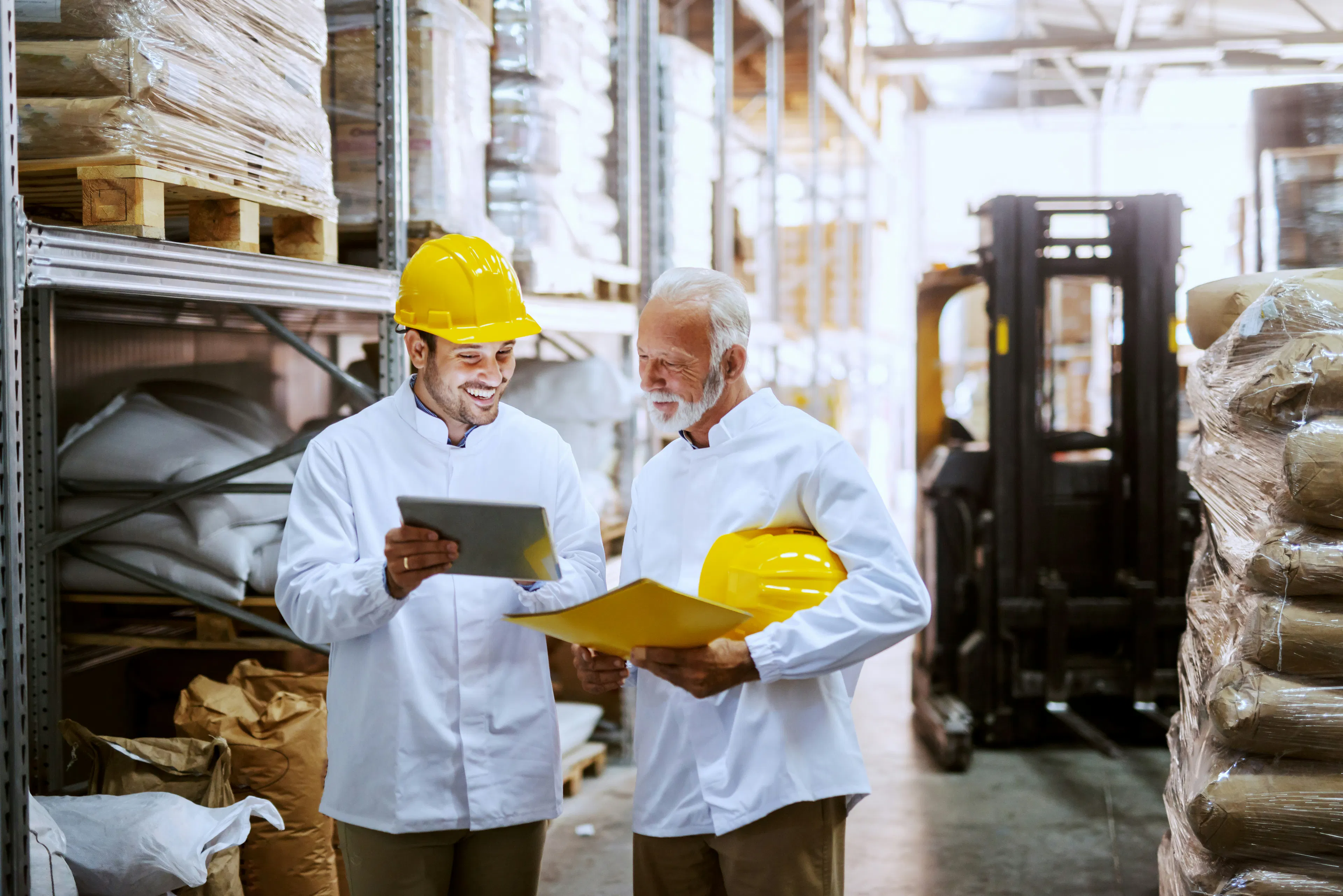 Two warehouse workers smiling at a tablet together.