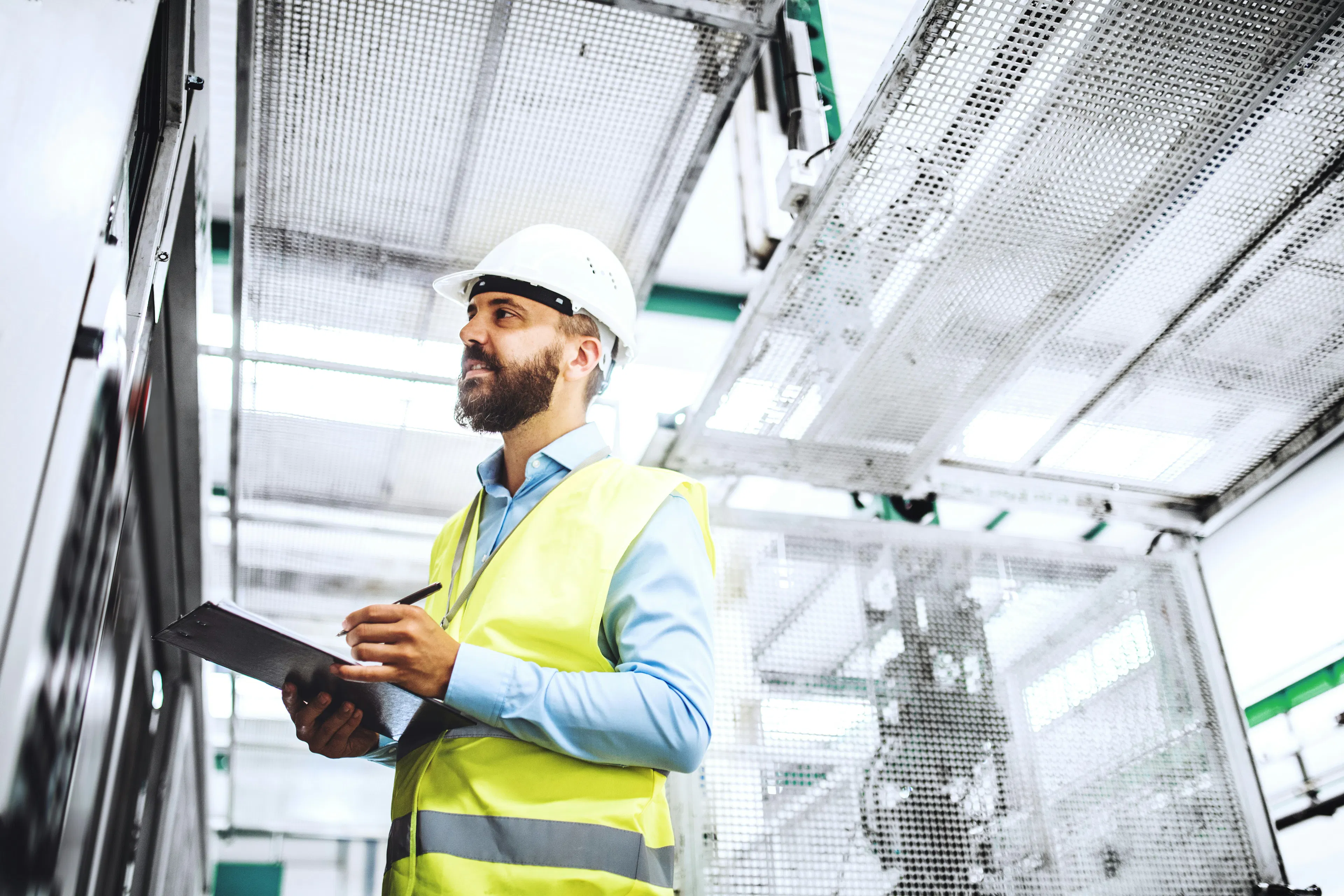 Worker in a hard hat writing on a clipboard in a factory