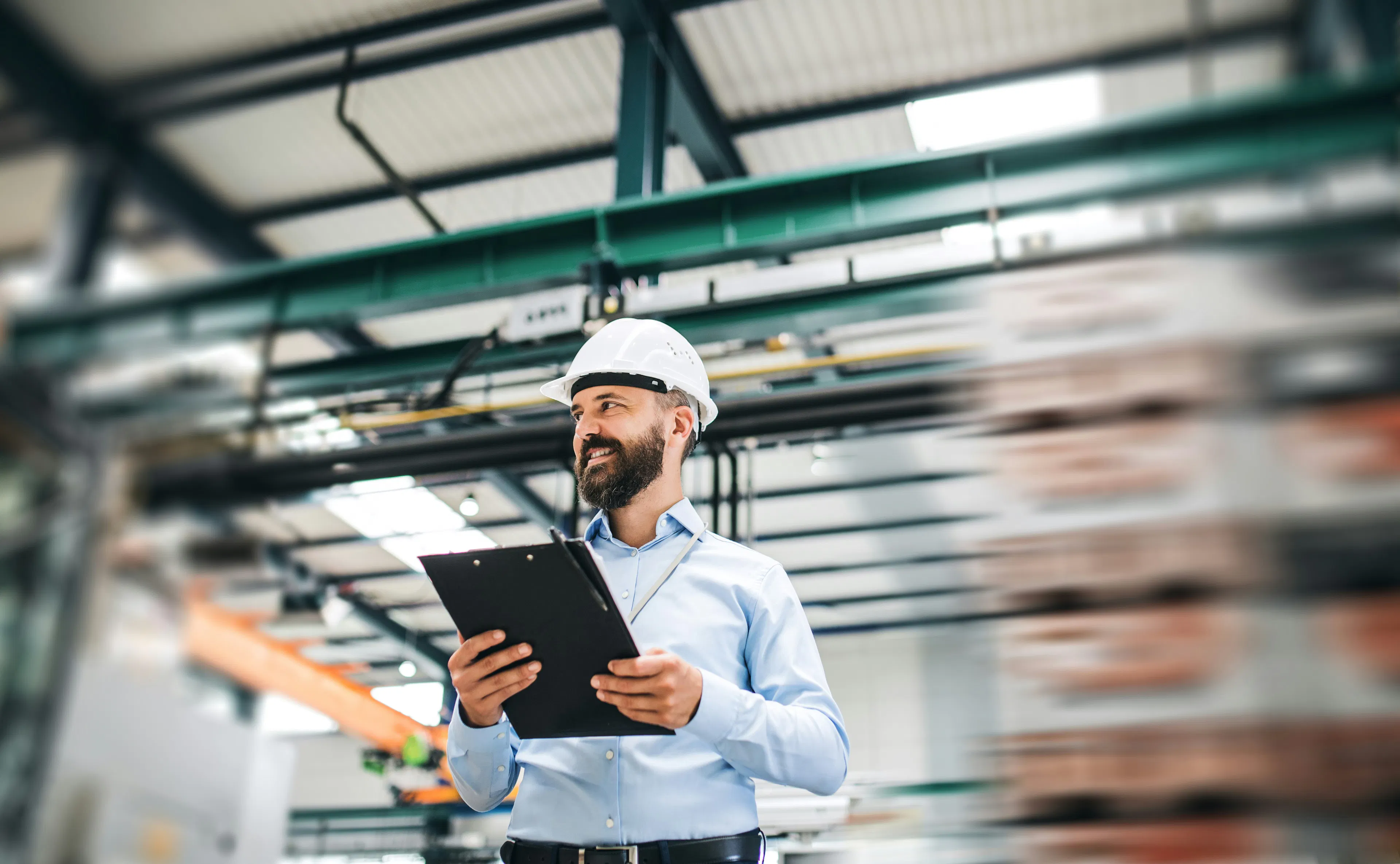 Supervisor in a hard hat holding a clipboard in a plant.