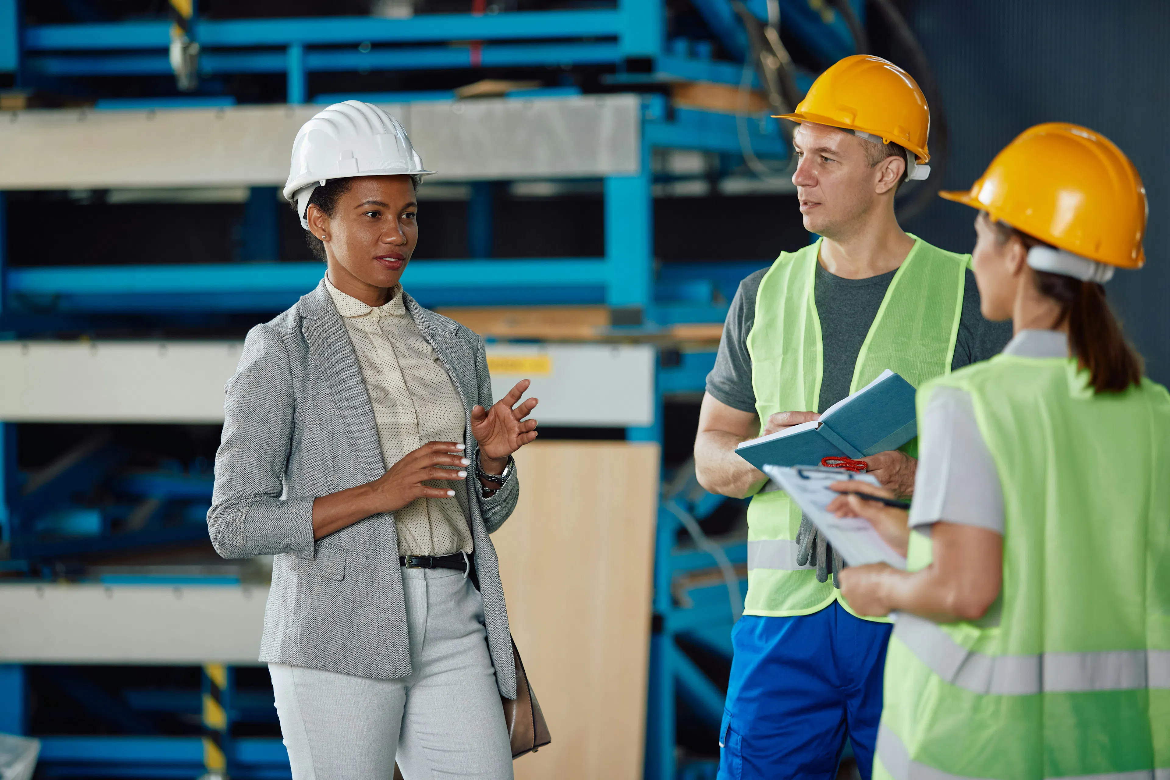Manager talking with two workers in hi-vis vests on a warehouse floor.