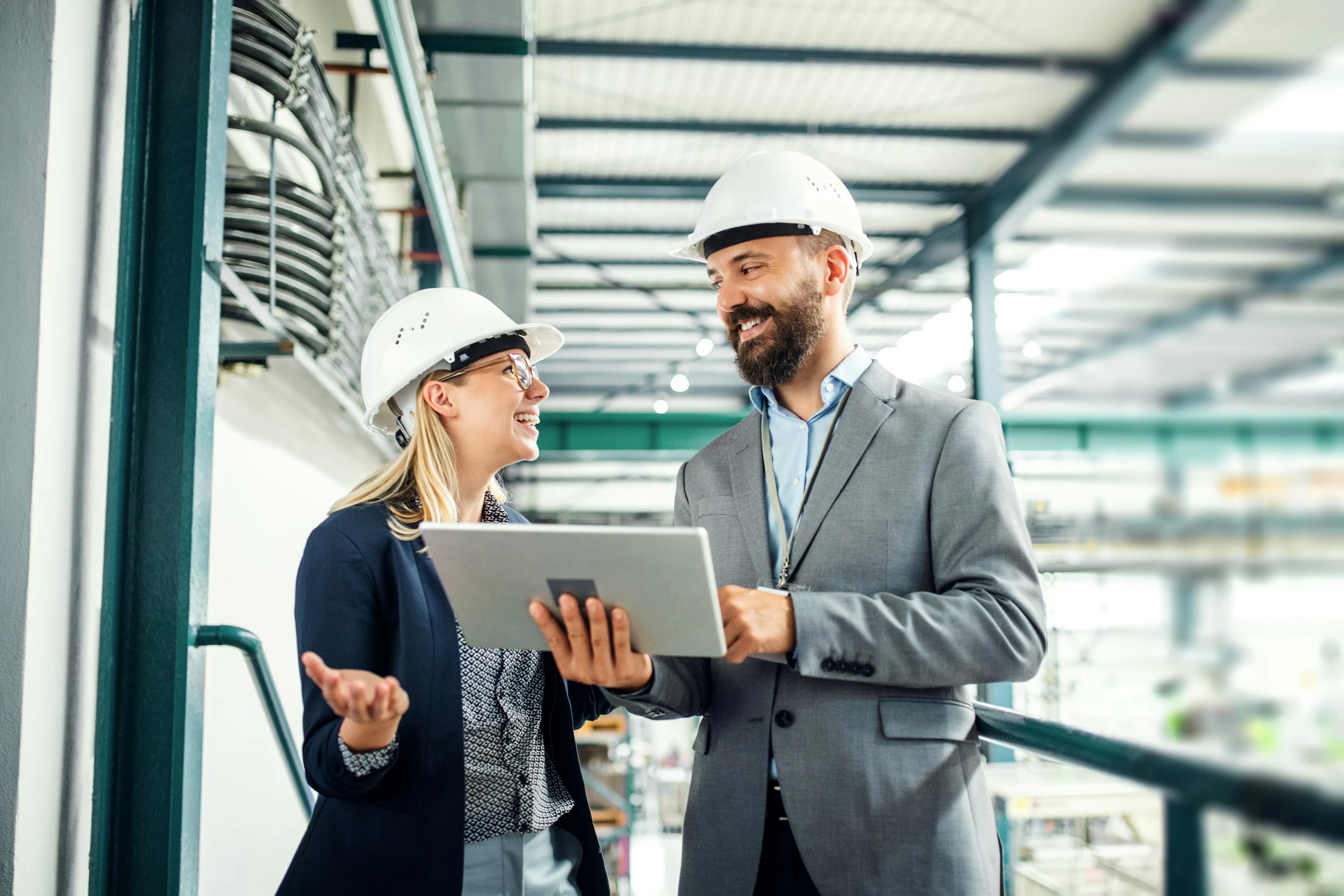 Two managers in hard hats reviewing a tablet in an industrial facility.