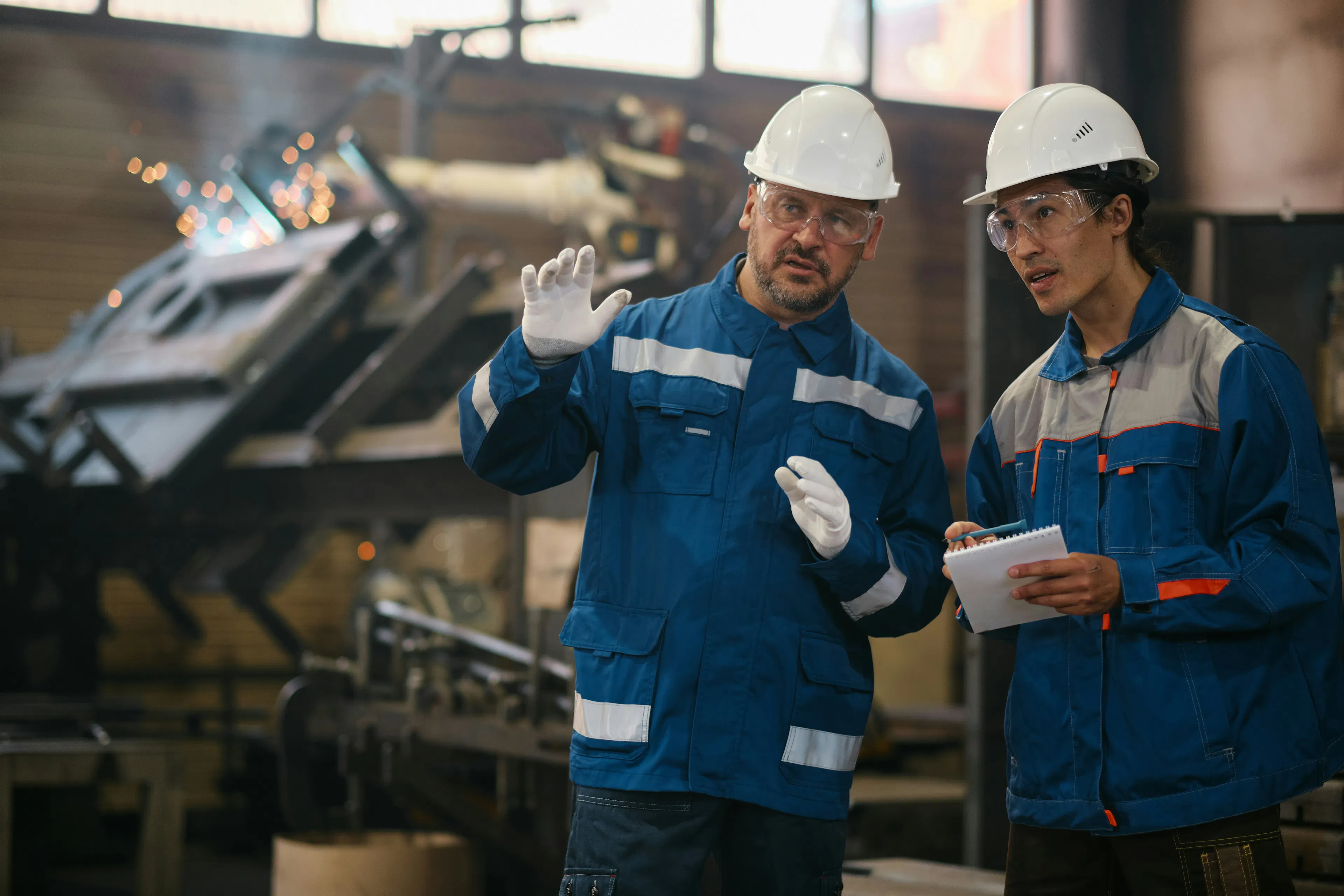 Two factory workers in hard hats discussing notes on the floor