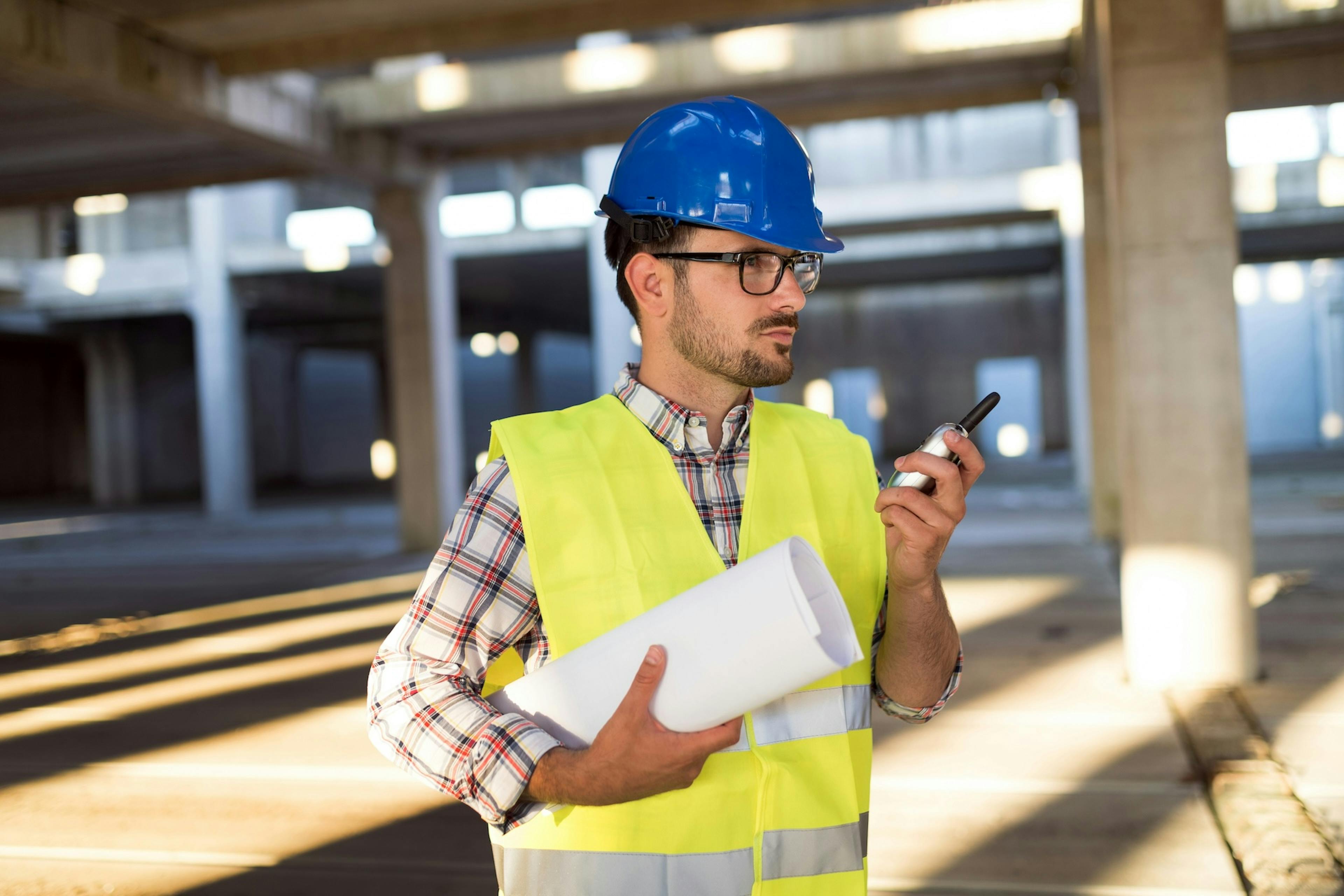 worker holding plans in one arm and a cellular in the other