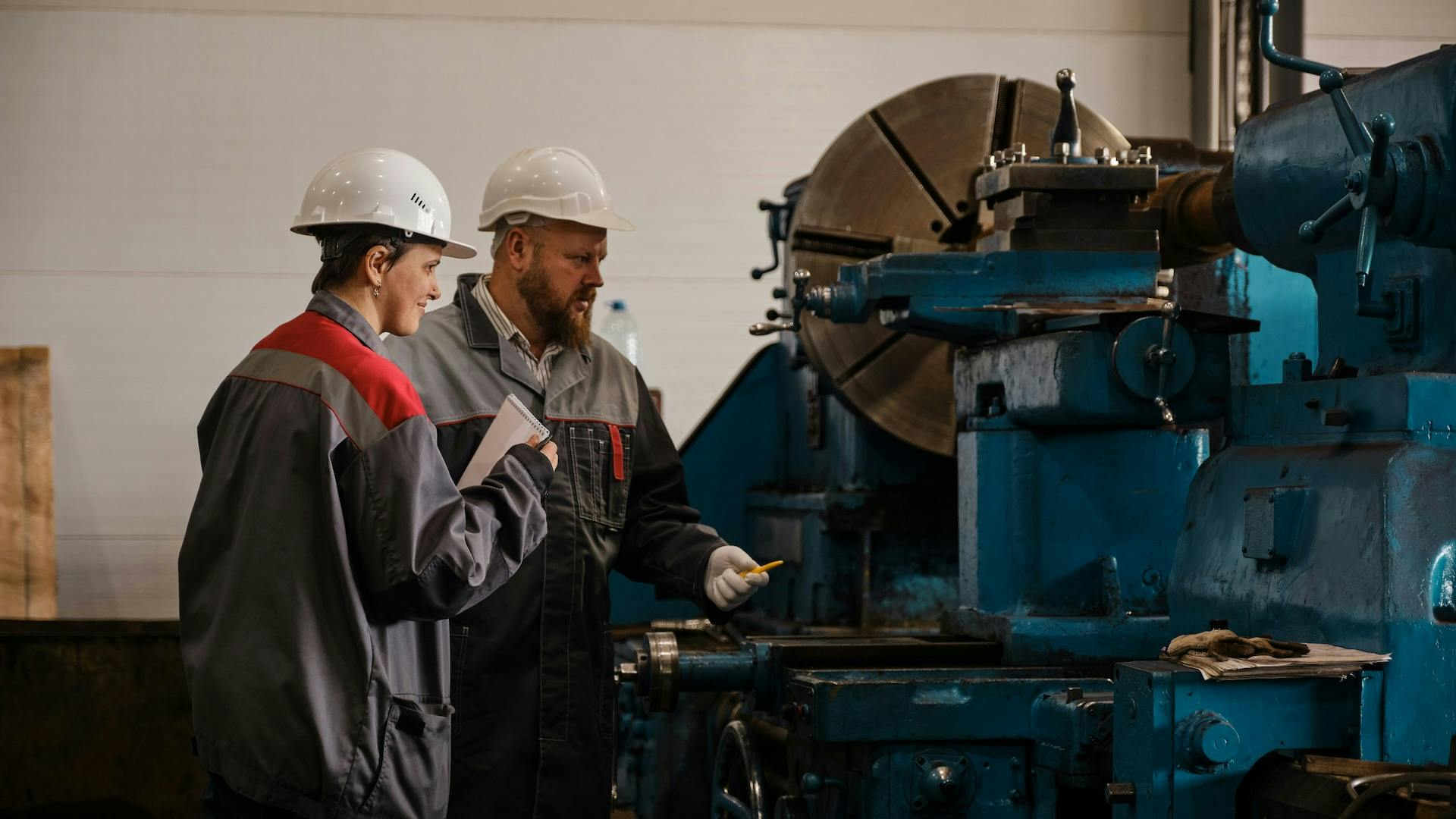 Two factory workers stand beside heavy industrial machinery