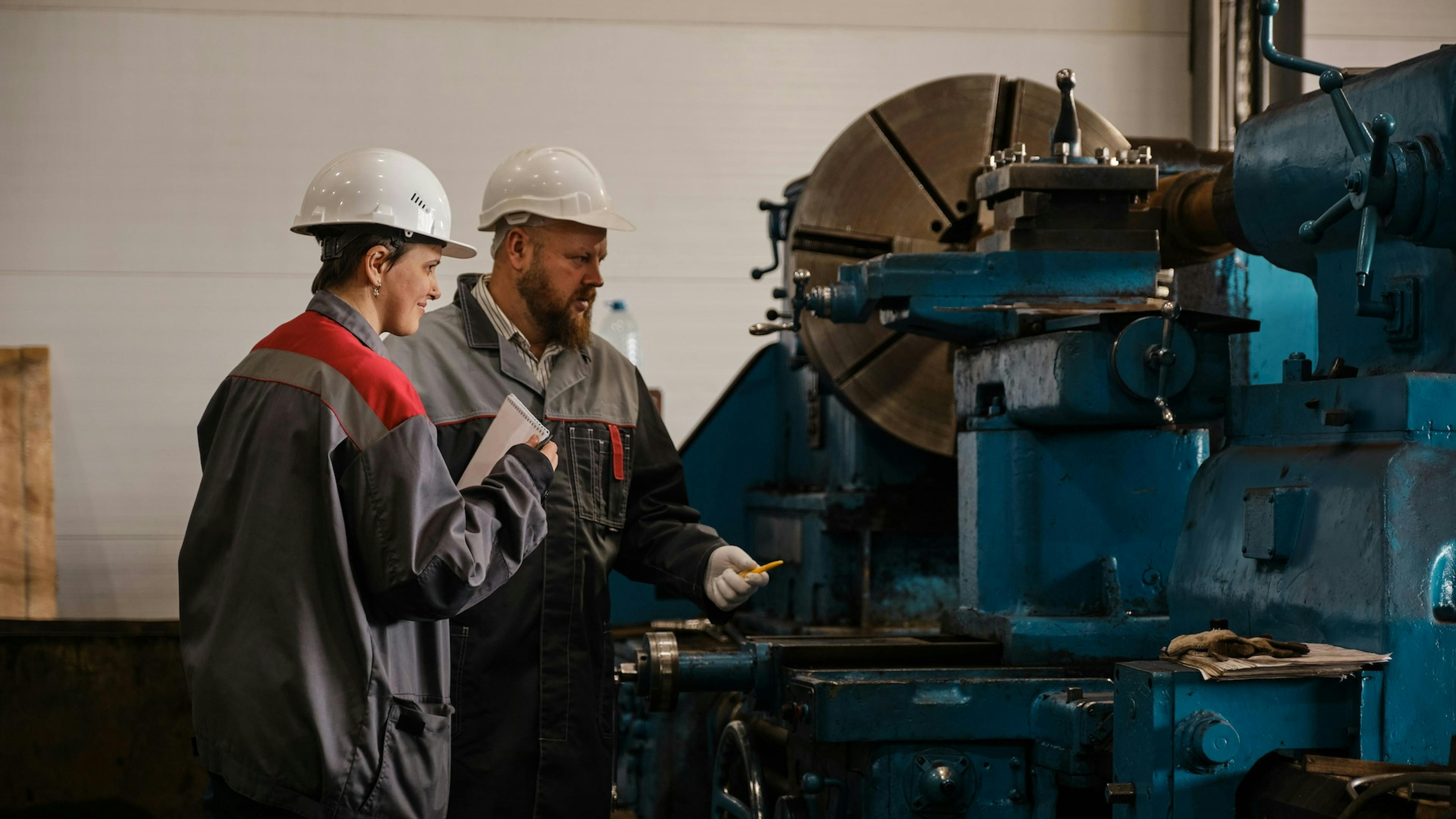 Two factory workers stand beside heavy industrial machinery