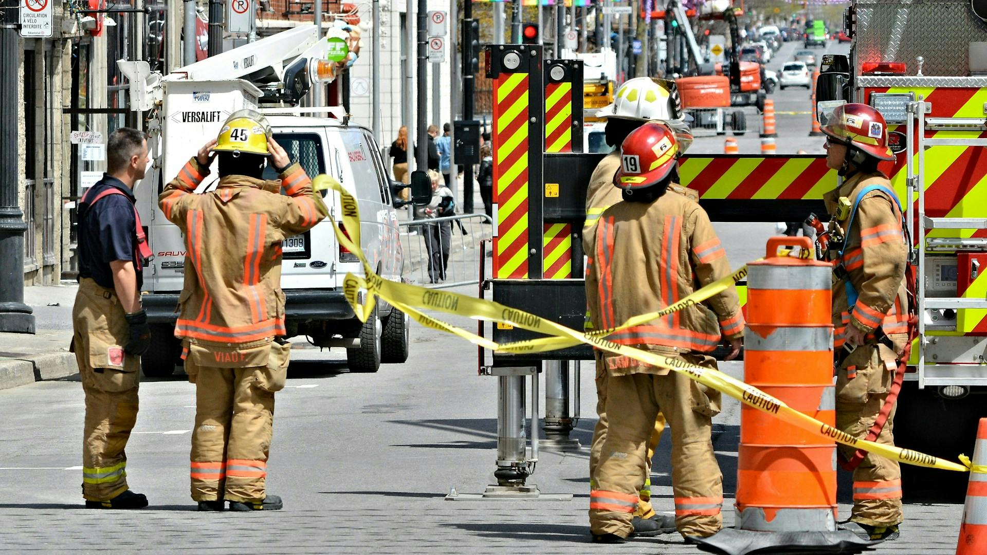 Firefighters wearing full protective gear and helmets standing behind yellow caution tape