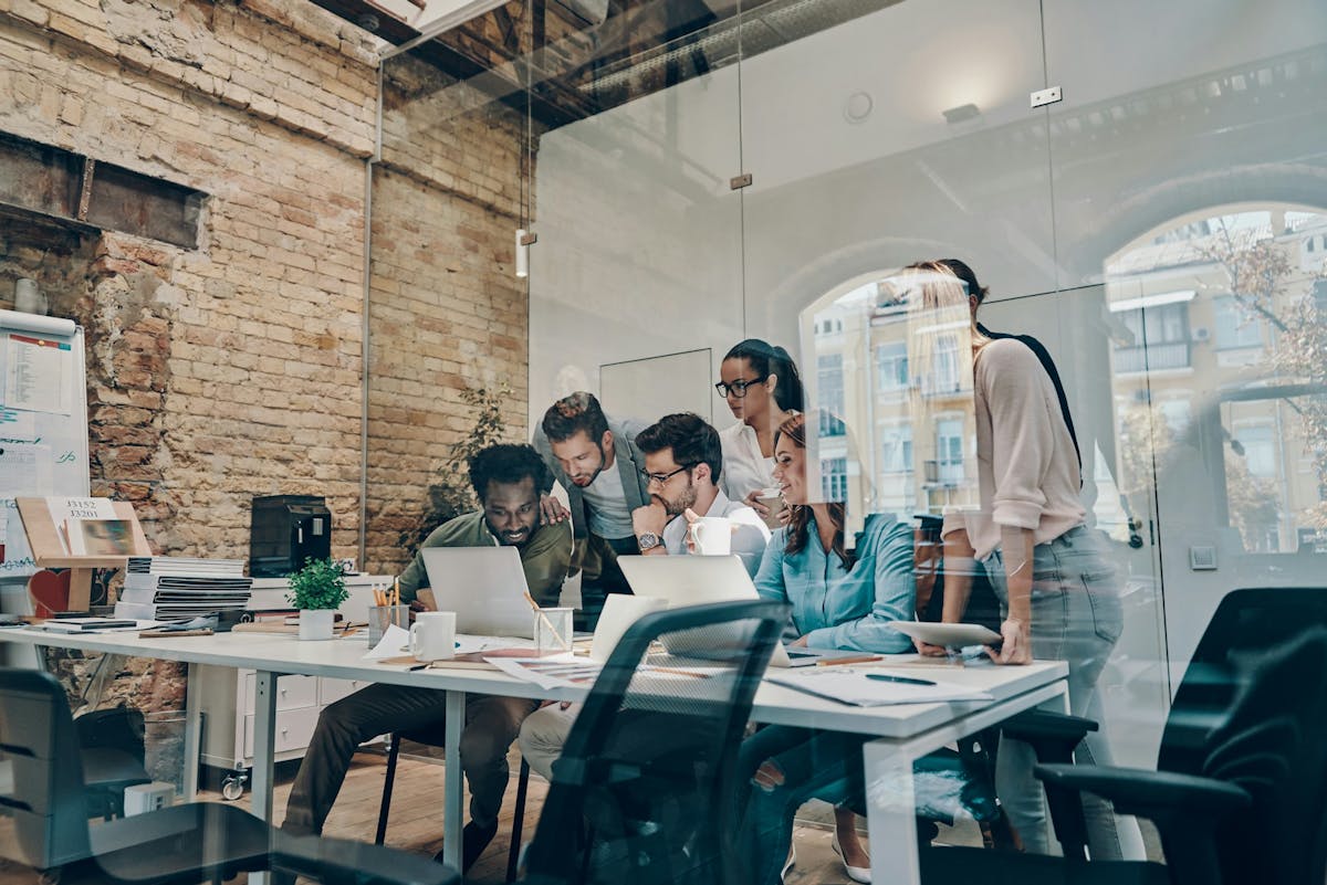 engaged employees sitting and standing in front of desk happily looking at computer screen