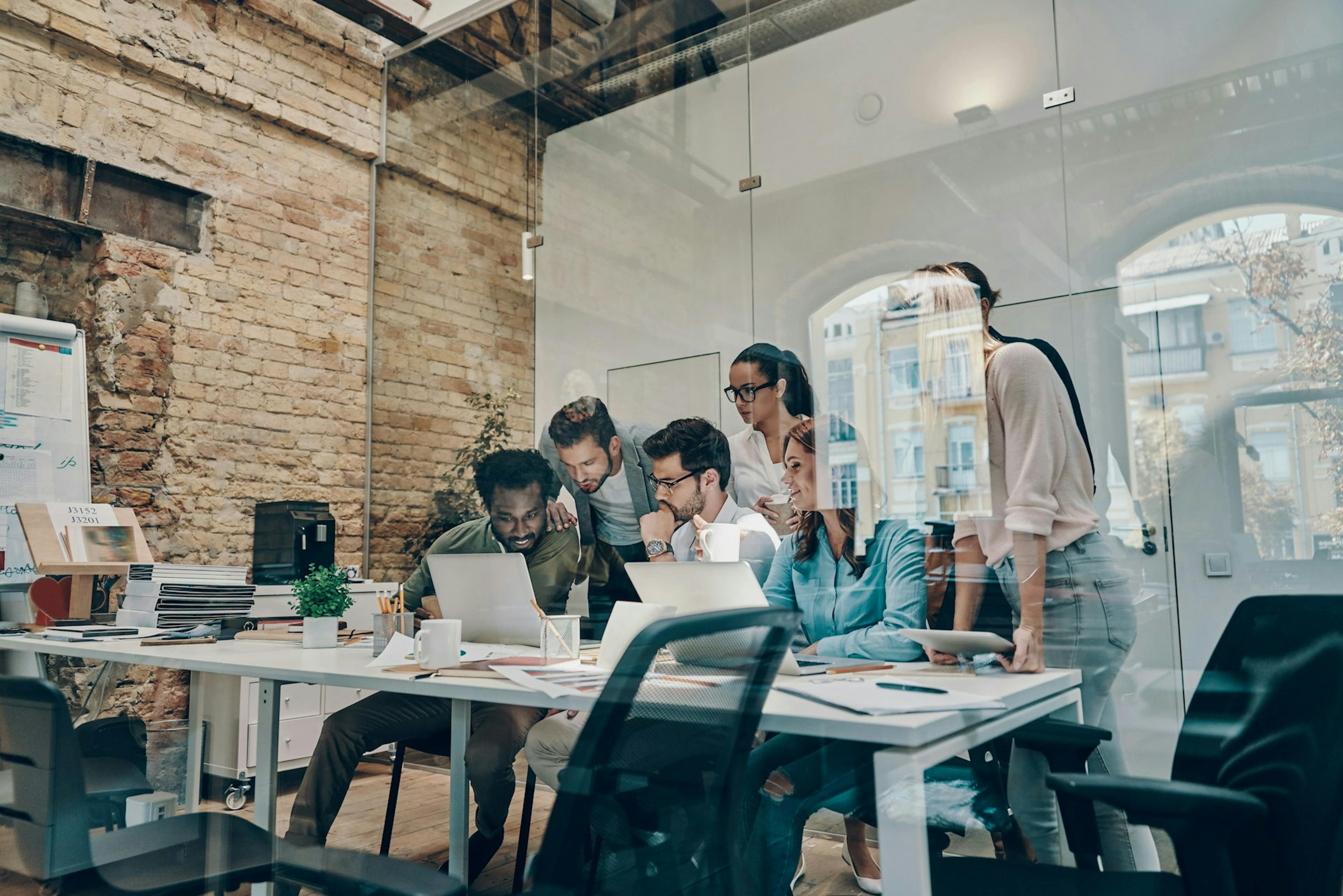 engaged employees sitting and standing in front of desk happily looking at computer screen