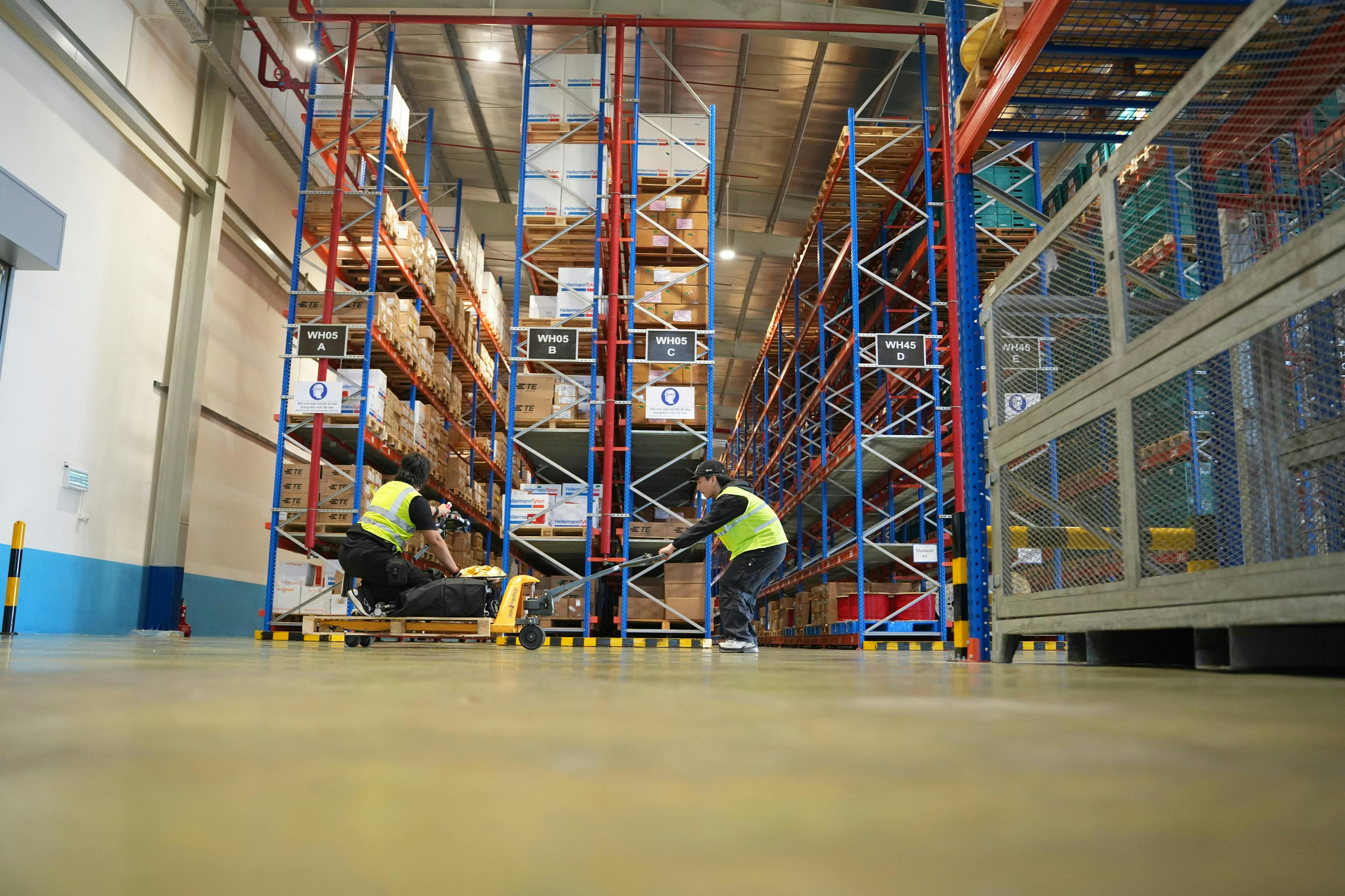 Warehouse workers in high-vis vests operating a pallet jack