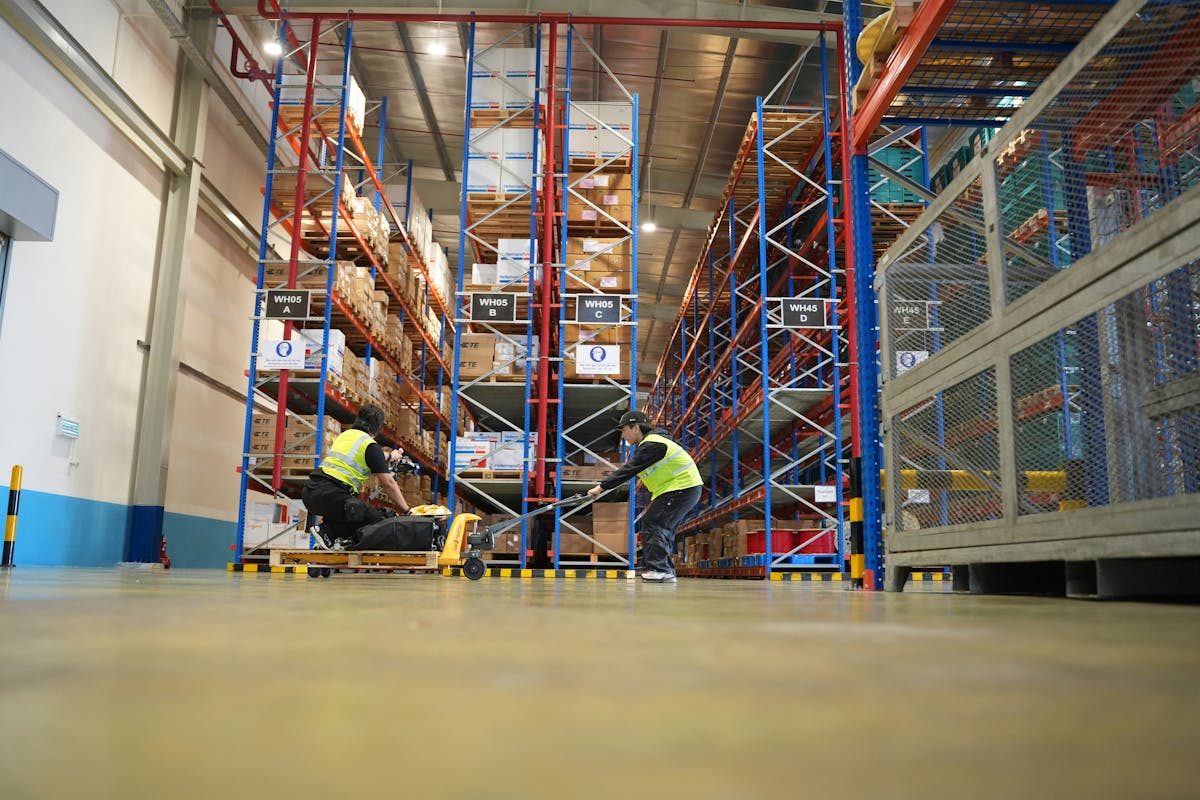 Warehouse workers in high-vis vests operating a pallet jack