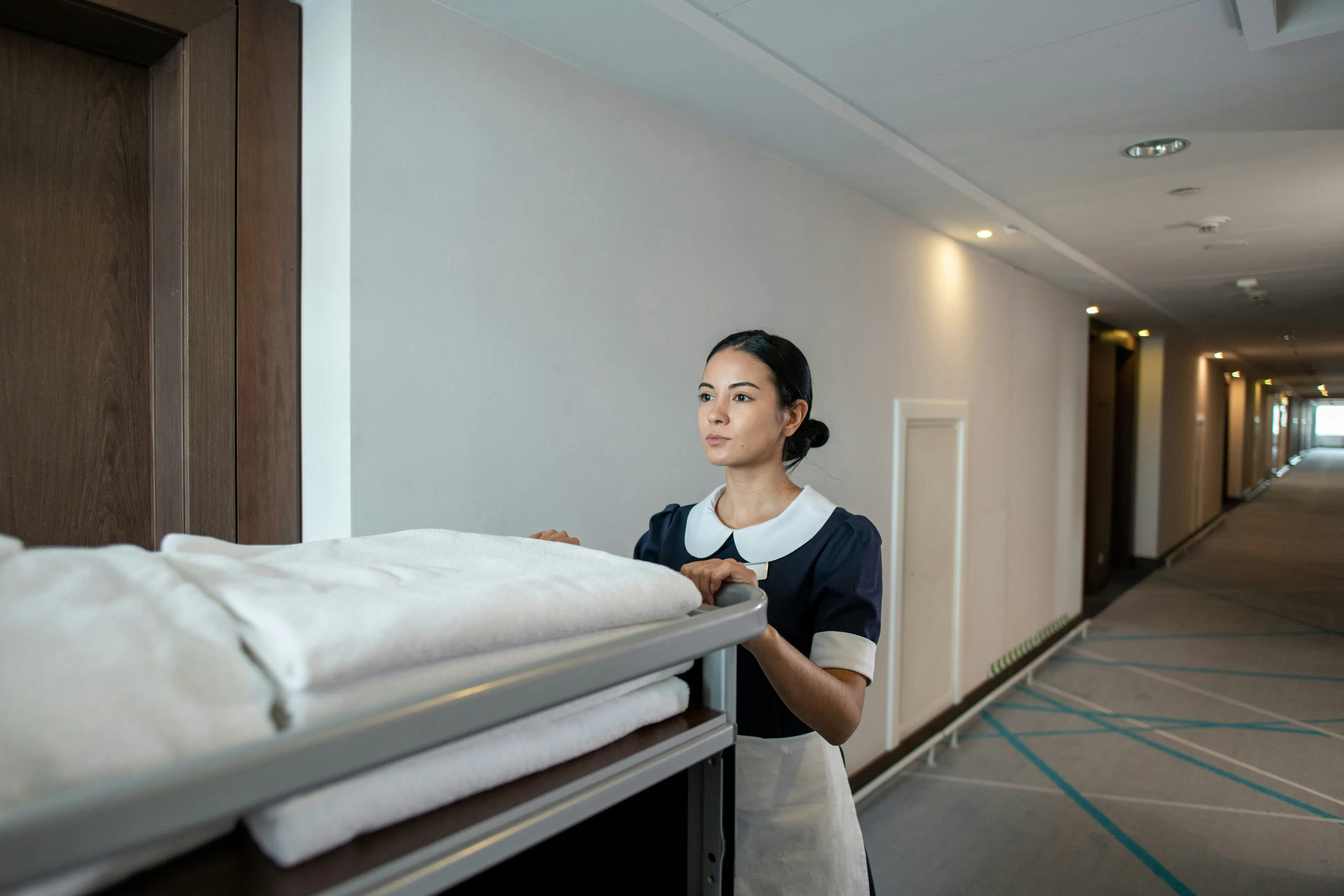 Hotel housekeeper pushing linen cart down corridor
