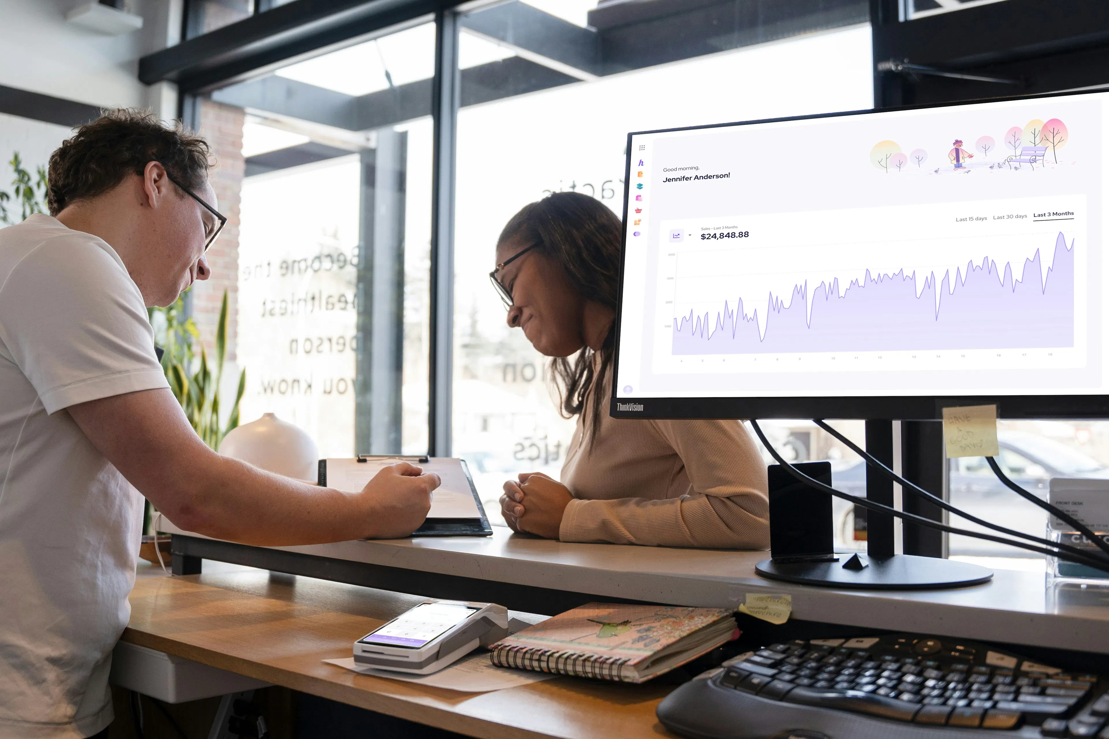 Two colleagues reviewing analytics data on large office monitor