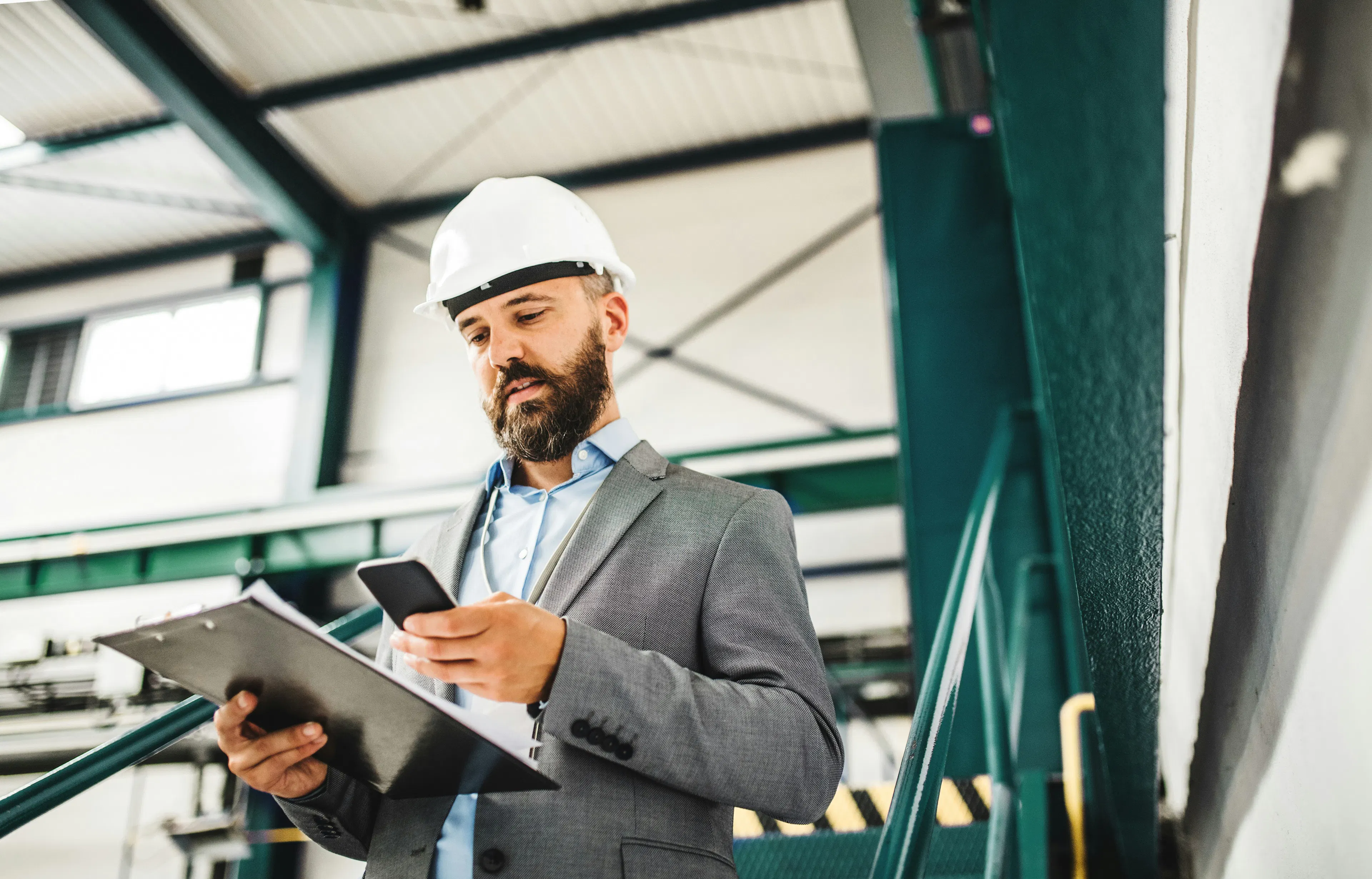 Supervisor in hard hat checking phone in factory